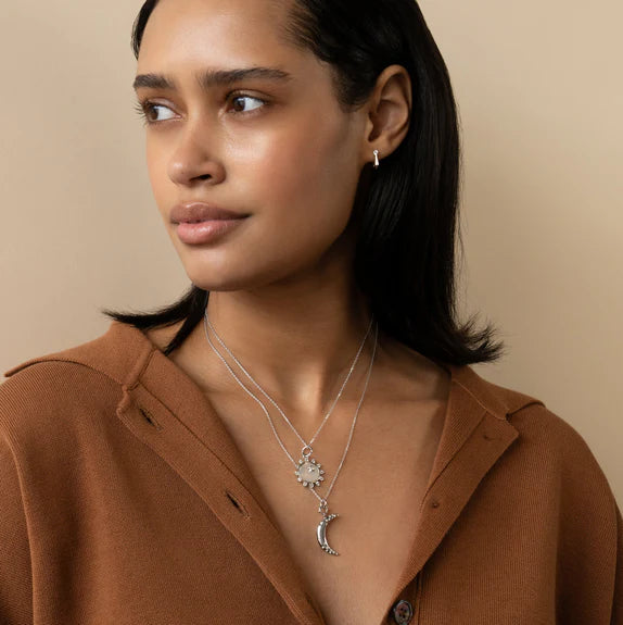 Woman wears sterling silver white mother of pearl and white sapphire sun pendant