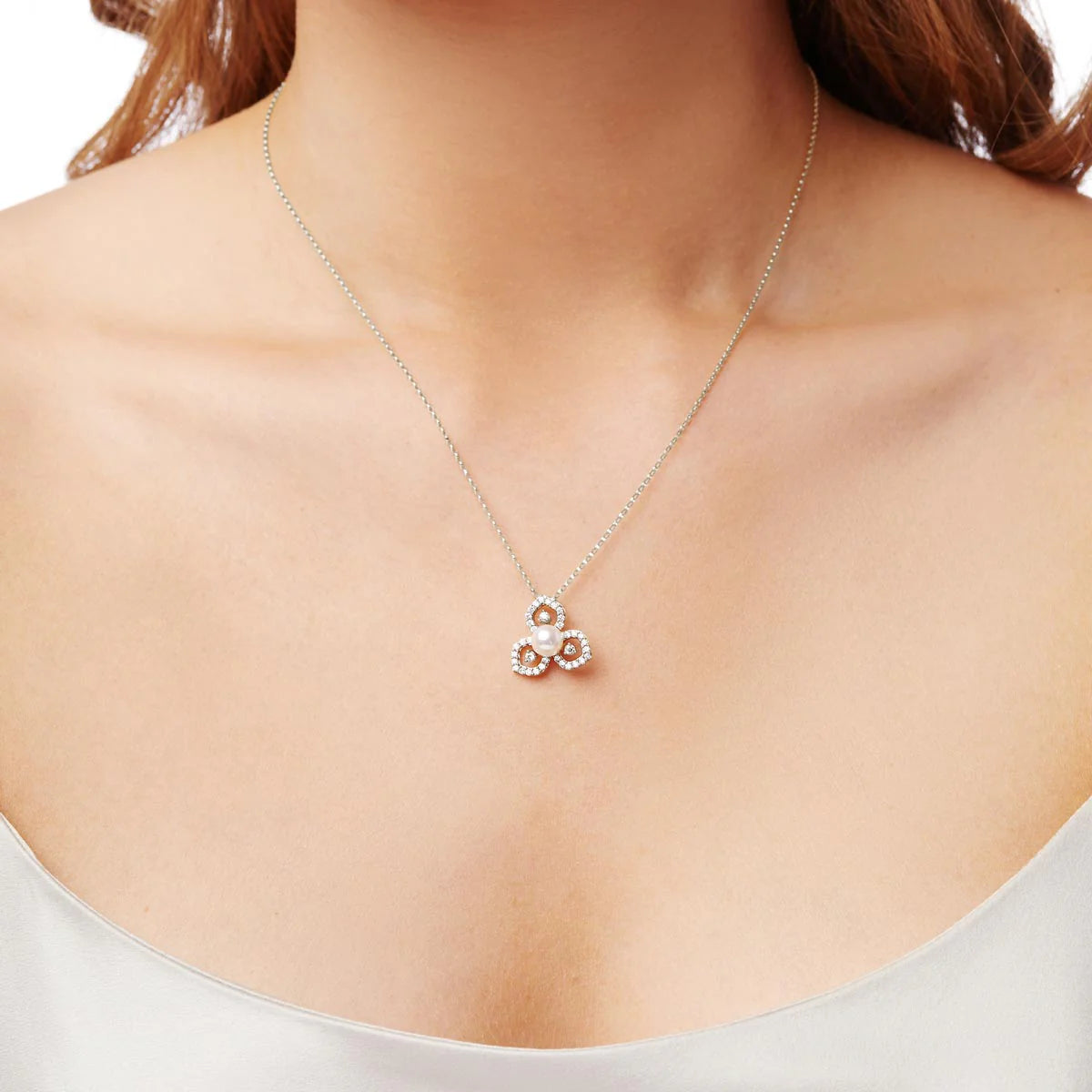 Woman wearing white gold cable chain necklace with pearl pendant surrounded by floral design diamond accents