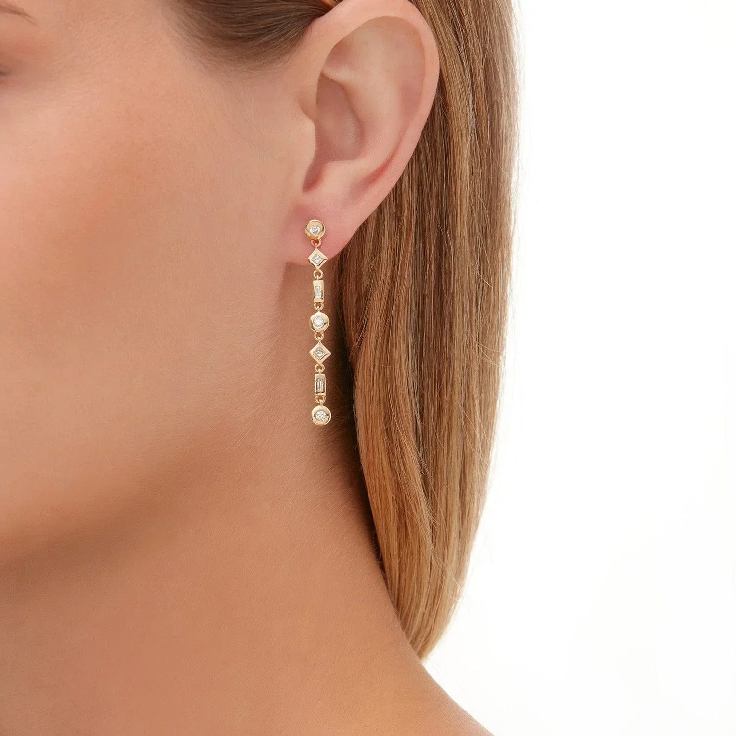 Woman wearing yellow gold drop earrings with mixed shape bezel set diamonds