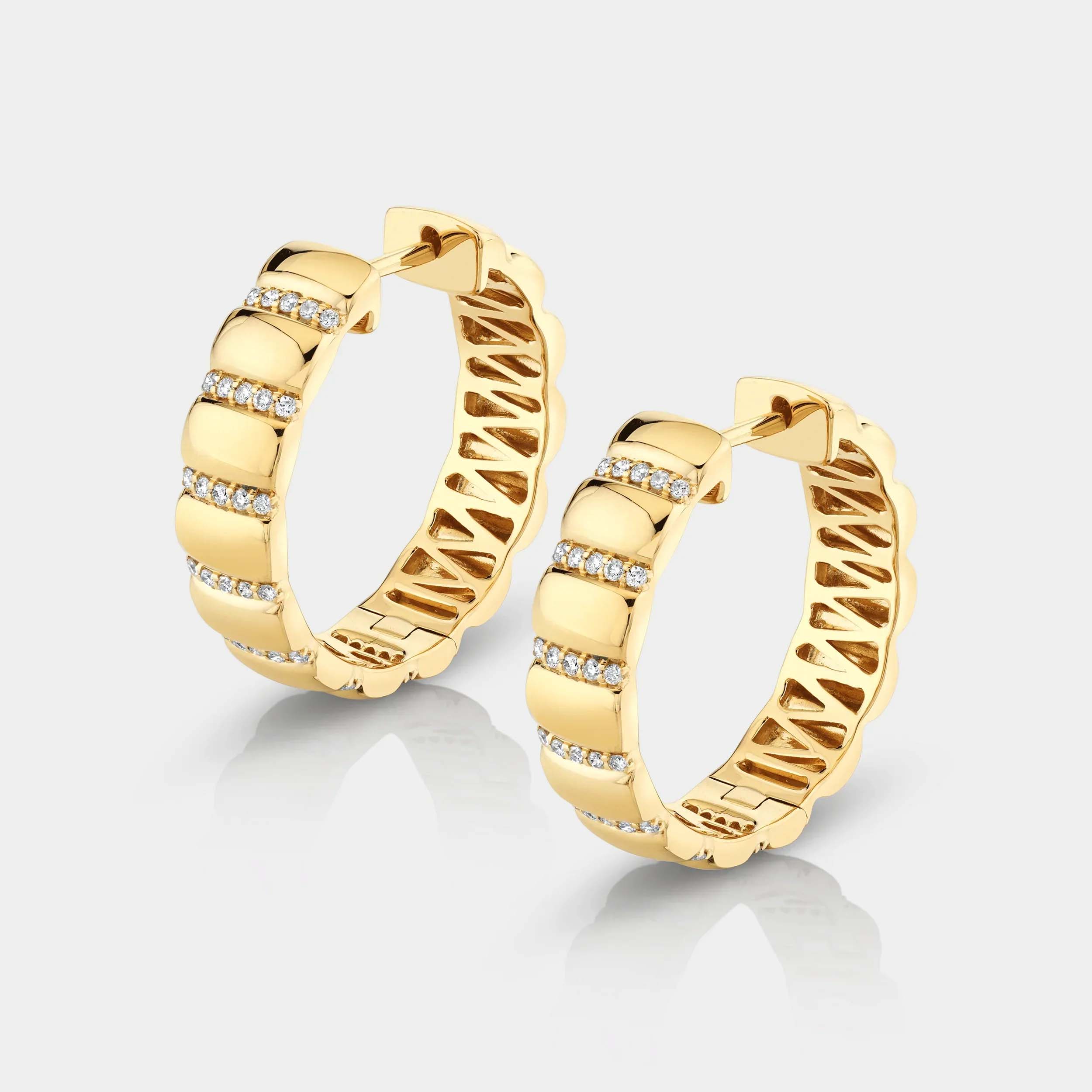 Yellow gold and diamond ribbed huggie earrings on grey background, side angle view