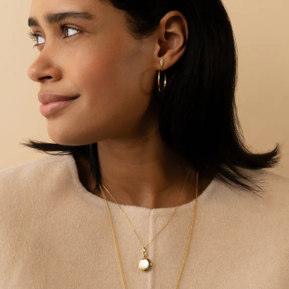 Woman wearing gold earrings and necklace against a beige background