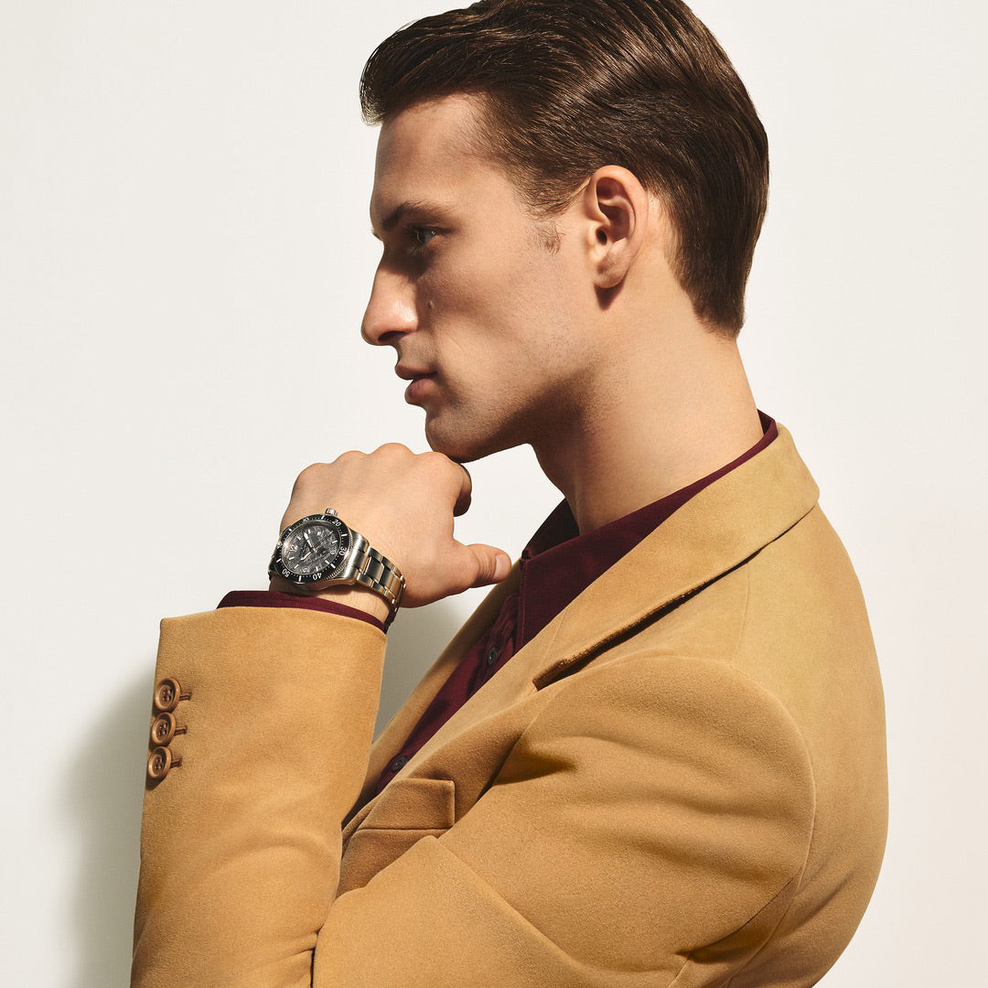 Man wearing a tan coat and watch, looking to the side against a light background