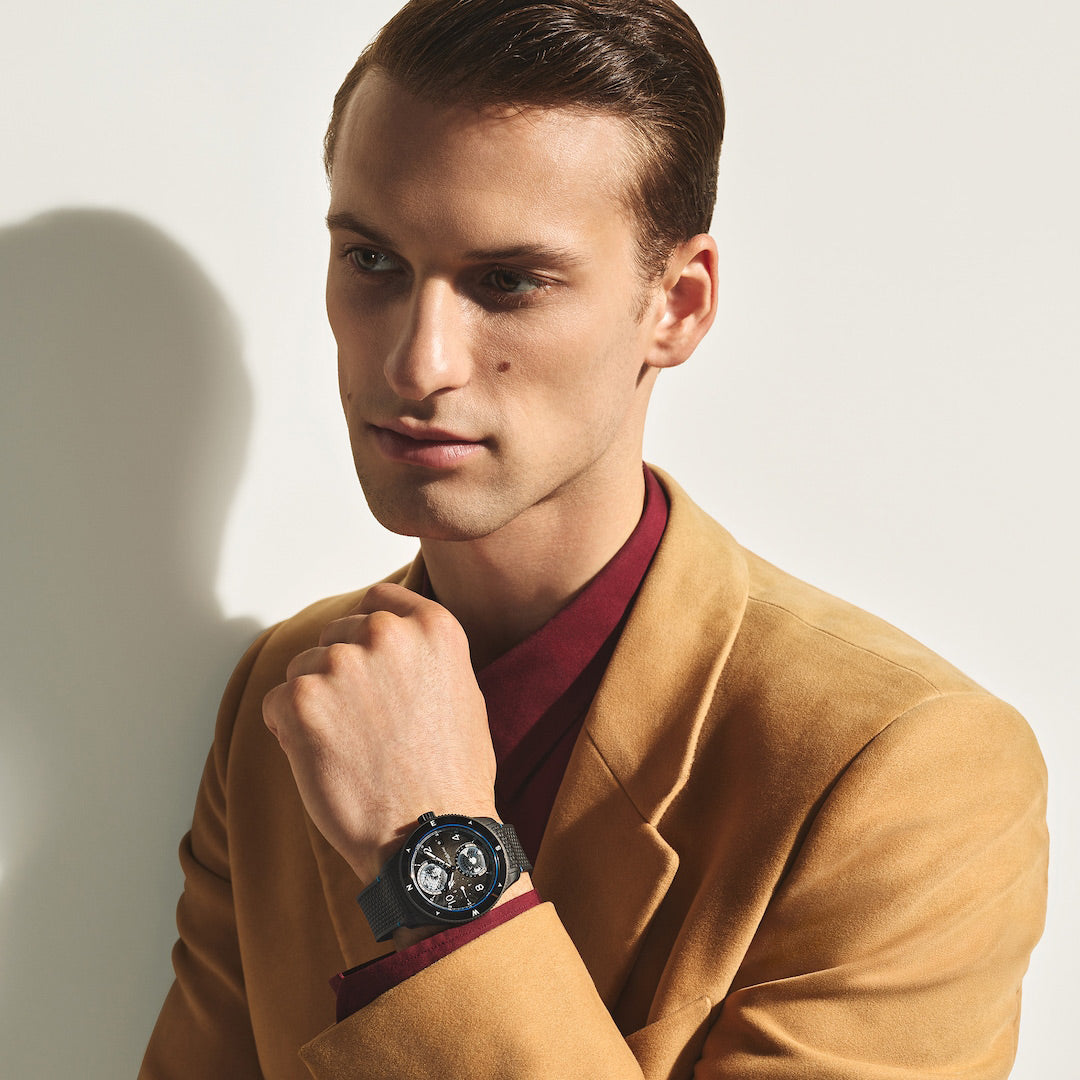 Man wearing a tan coat and red shirt with a watch, against a white background
