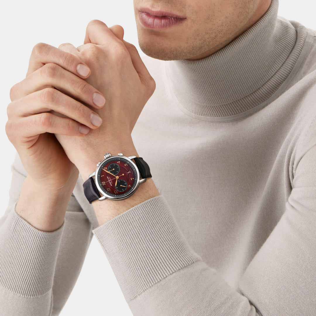 Person wearing a watch with a red face and black strap on a light background