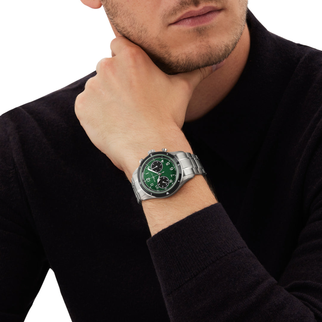 Man wearing a watch with a green face and silver case on a white background