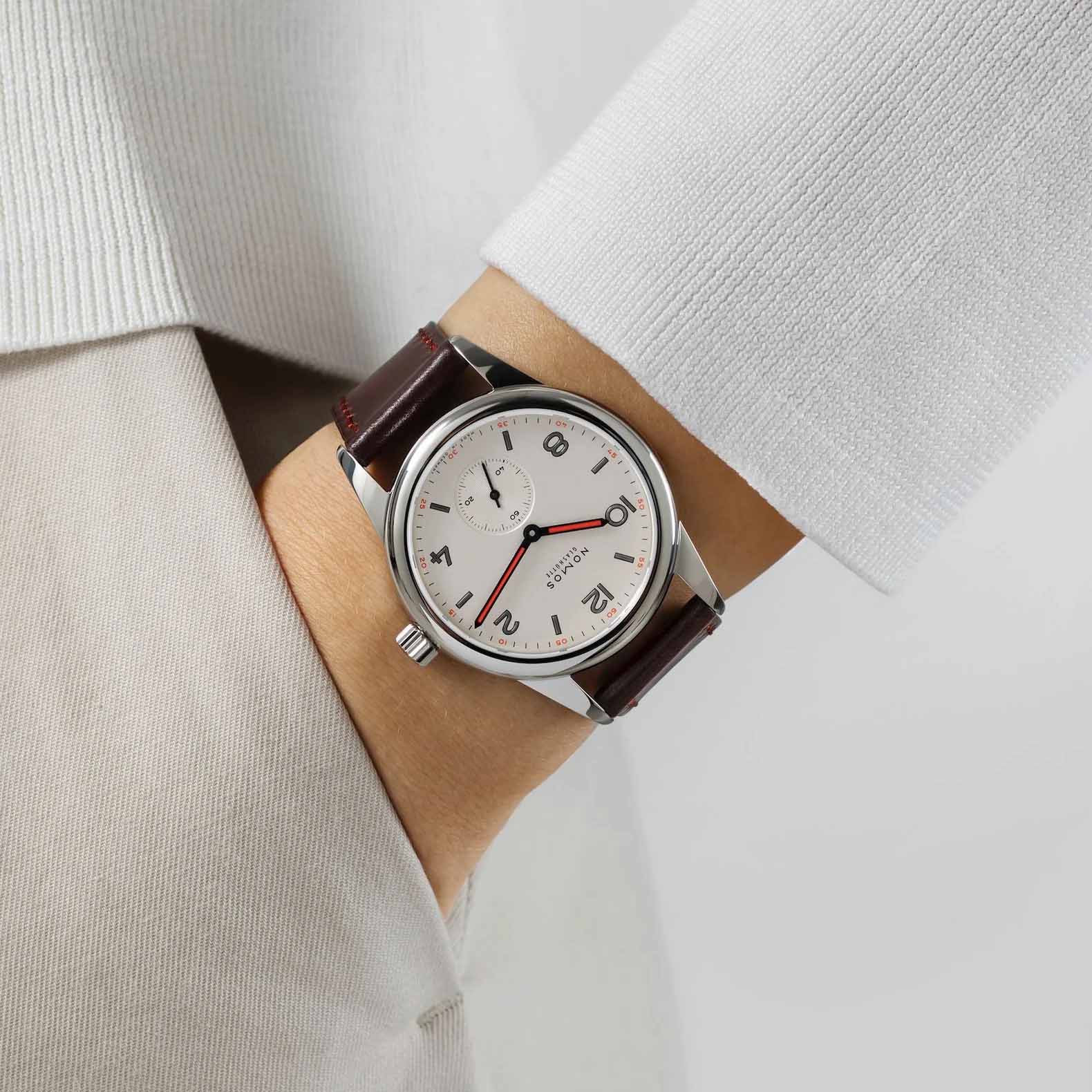 Man wearing NOMOS Glashütte Club 36mm watch with white silver-plated dial, black and red hands, and brown Horween leather strap