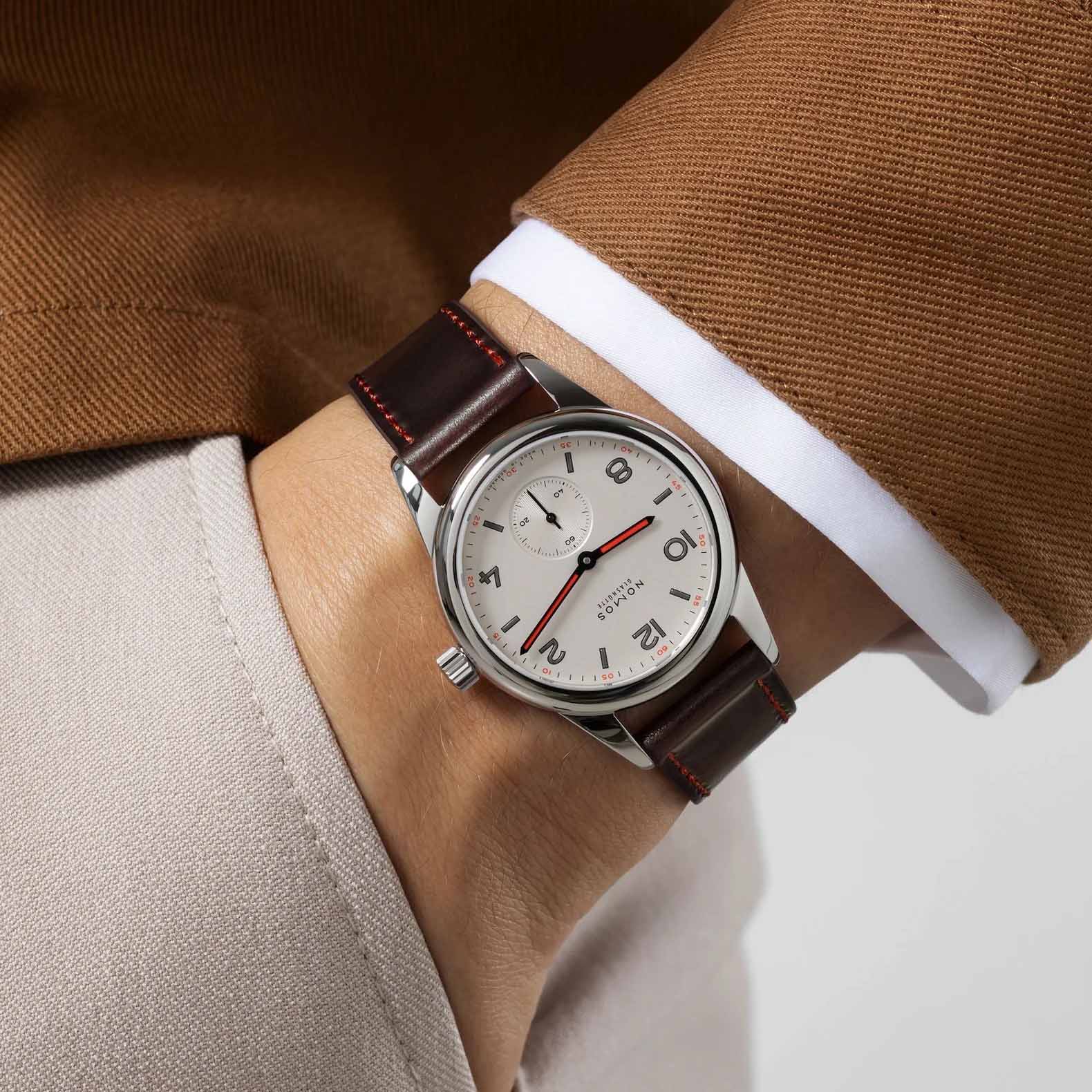 Man wearing NOMOS Glashütte Club 36mm watch with white silver-plated dial, black and red hands, and brown Horween leather strap