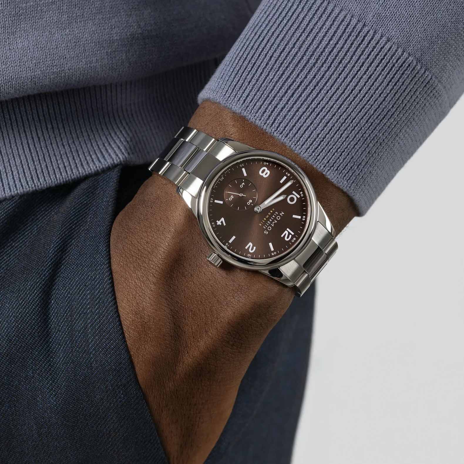 Man wearing NOMOS Glashütte Club Sport Neomatik 39mm watch with tabac brown sunburst dial, luminous hands, and stainless steel bracelet.