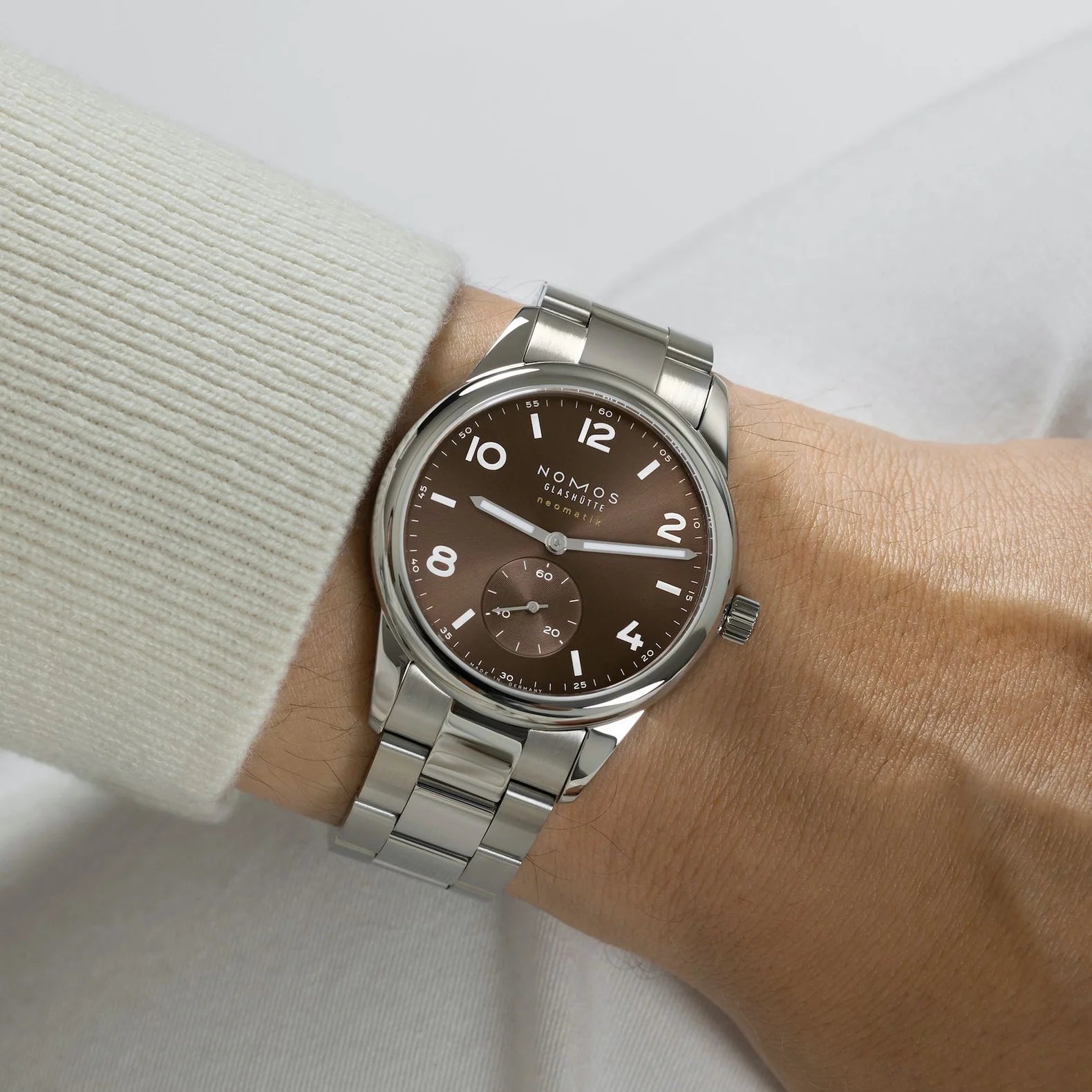 Man wearing NOMOS Glashütte Club Sport Neomatik 39mm watch with tabac brown sunburst dial, luminous hands, and stainless steel bracelet.