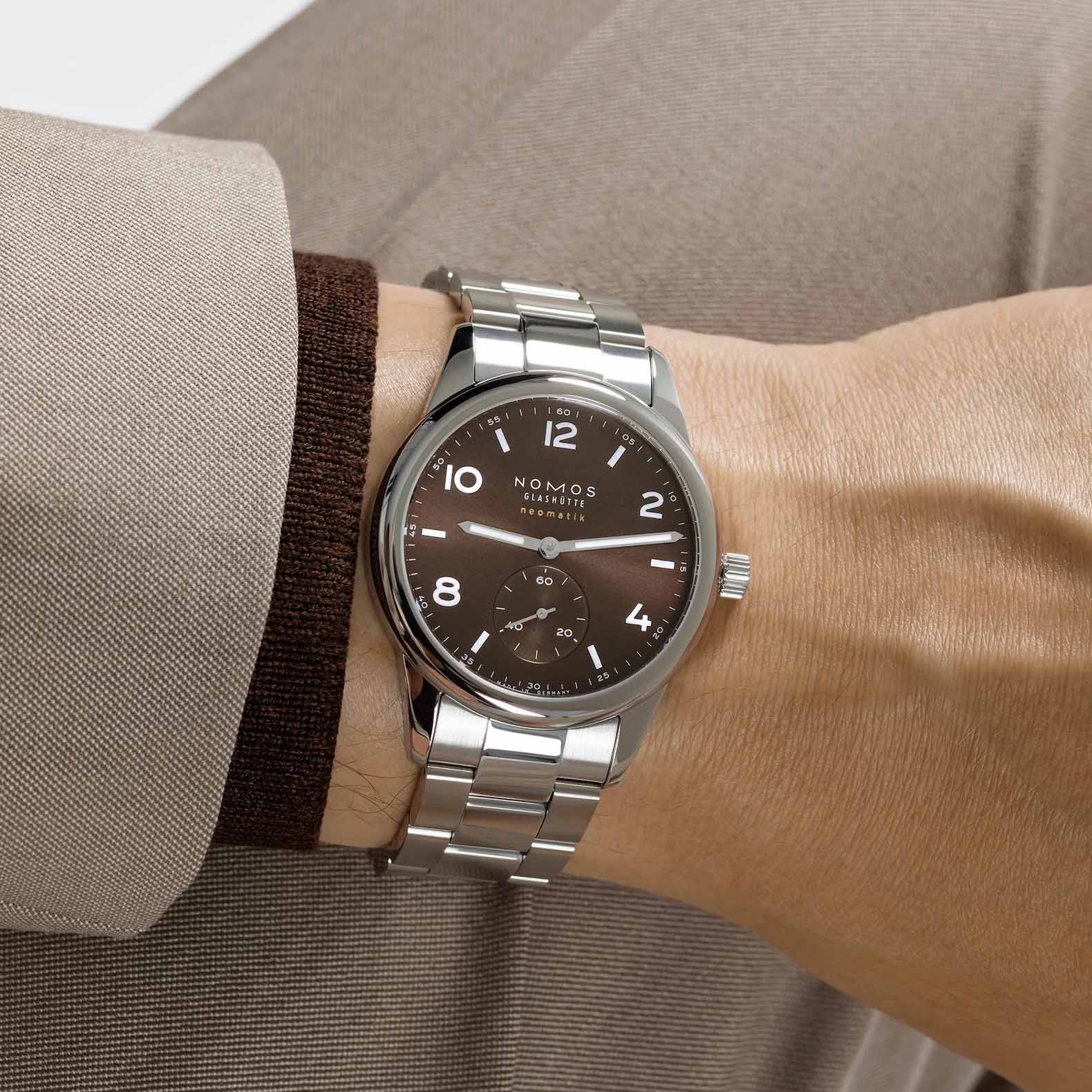 Man wearing NOMOS Glashütte Club Sport Neomatik 39mm watch with tabac brown sunburst dial, luminous hands, and stainless steel bracelet.