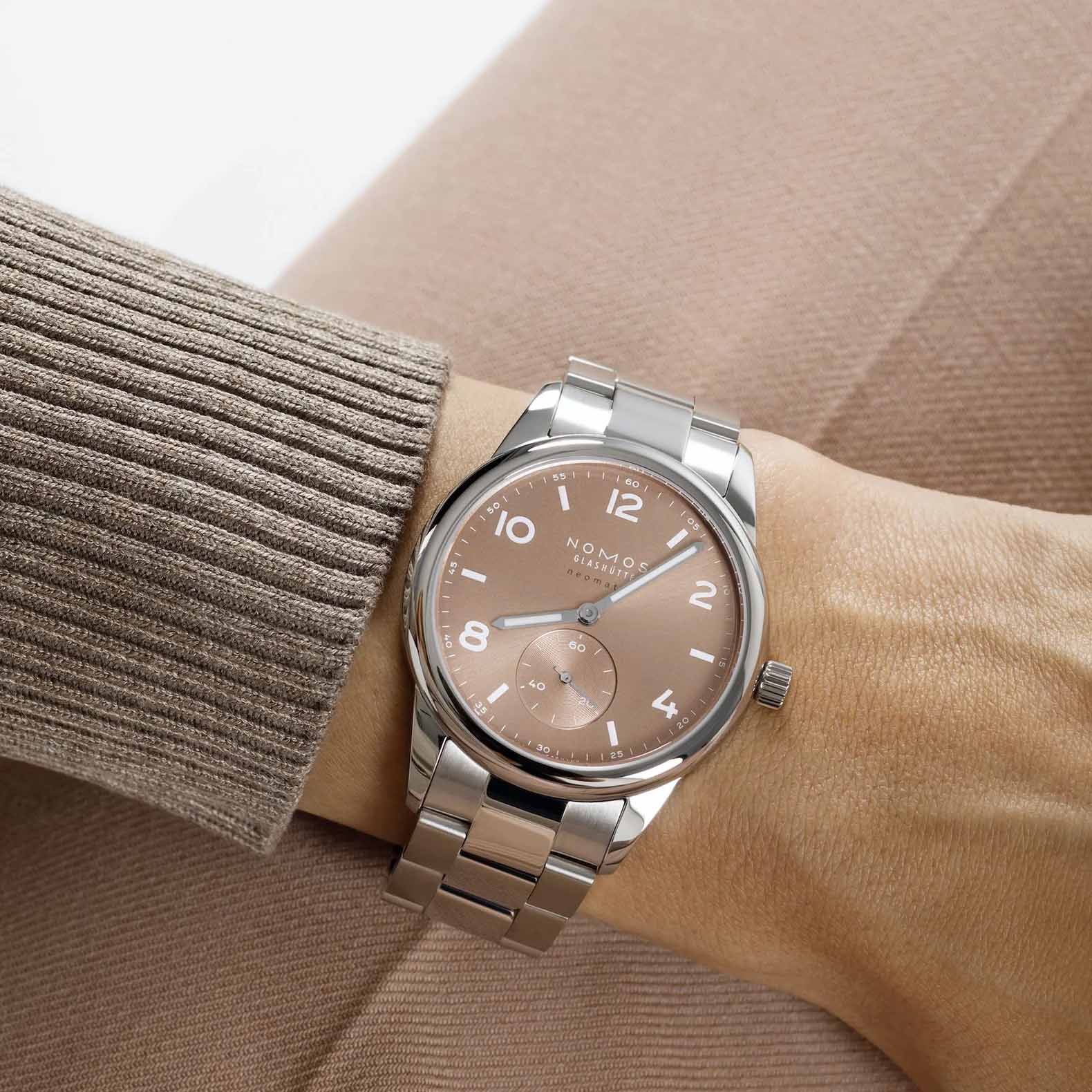 Man wearing NOMOS Glashütte Club Sport Neomatik 39mm watch with ember beige-gold sunburst dial, luminous hands, and stainless steel bracelet.