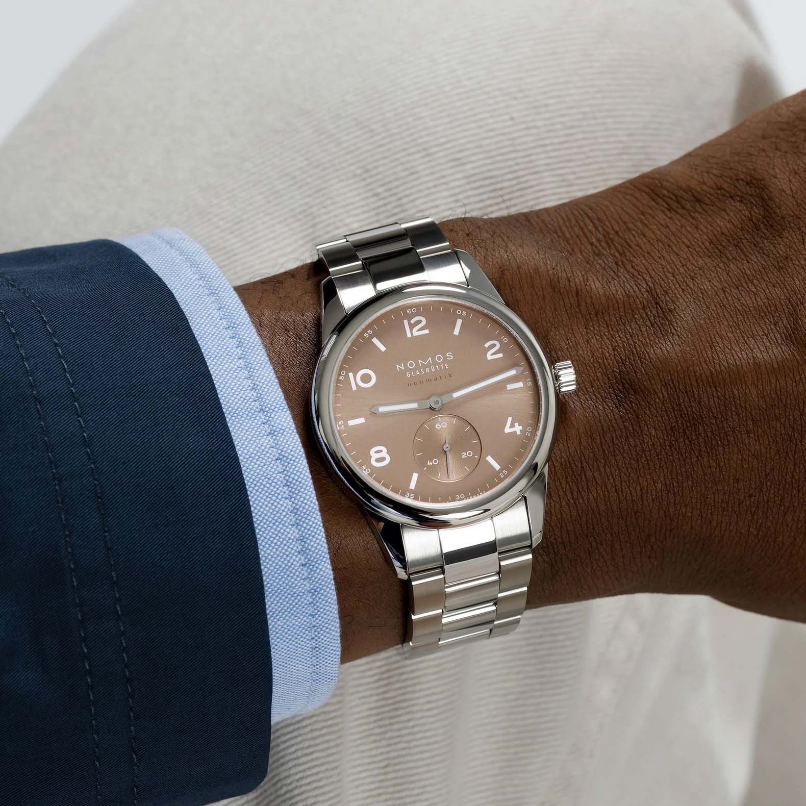 NOMOS Glashütte Club Sport Neomatik 39mm watch with ember beige-gold sunburst dial, luminous hands, and stainless steel bracelet.