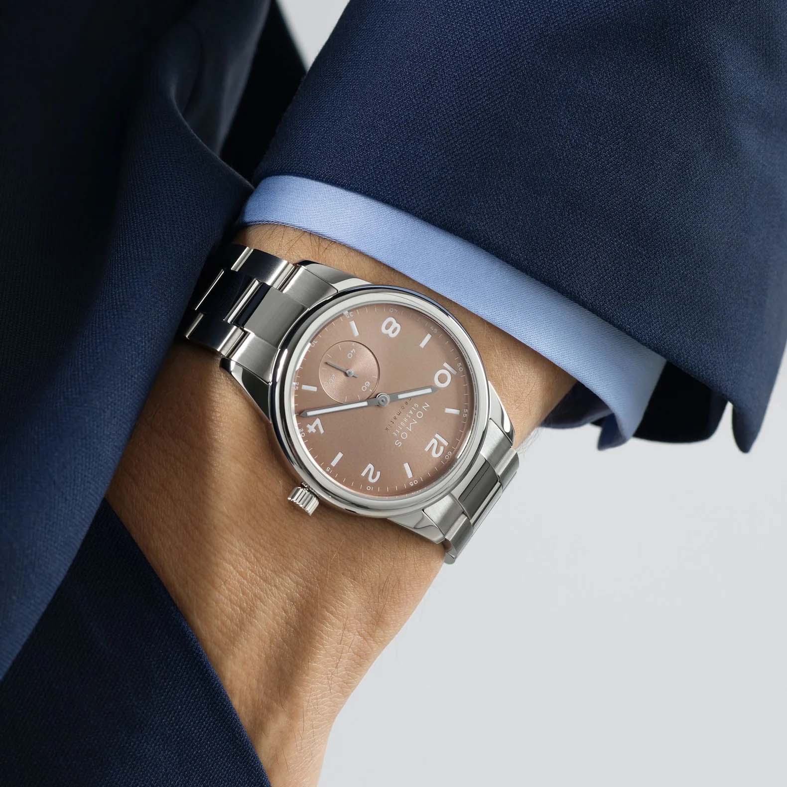 Man wearing NOMOS Glashütte Club Sport Neomatik 39mm watch with ember beige-gold sunburst dial, luminous hands, and stainless steel bracelet.