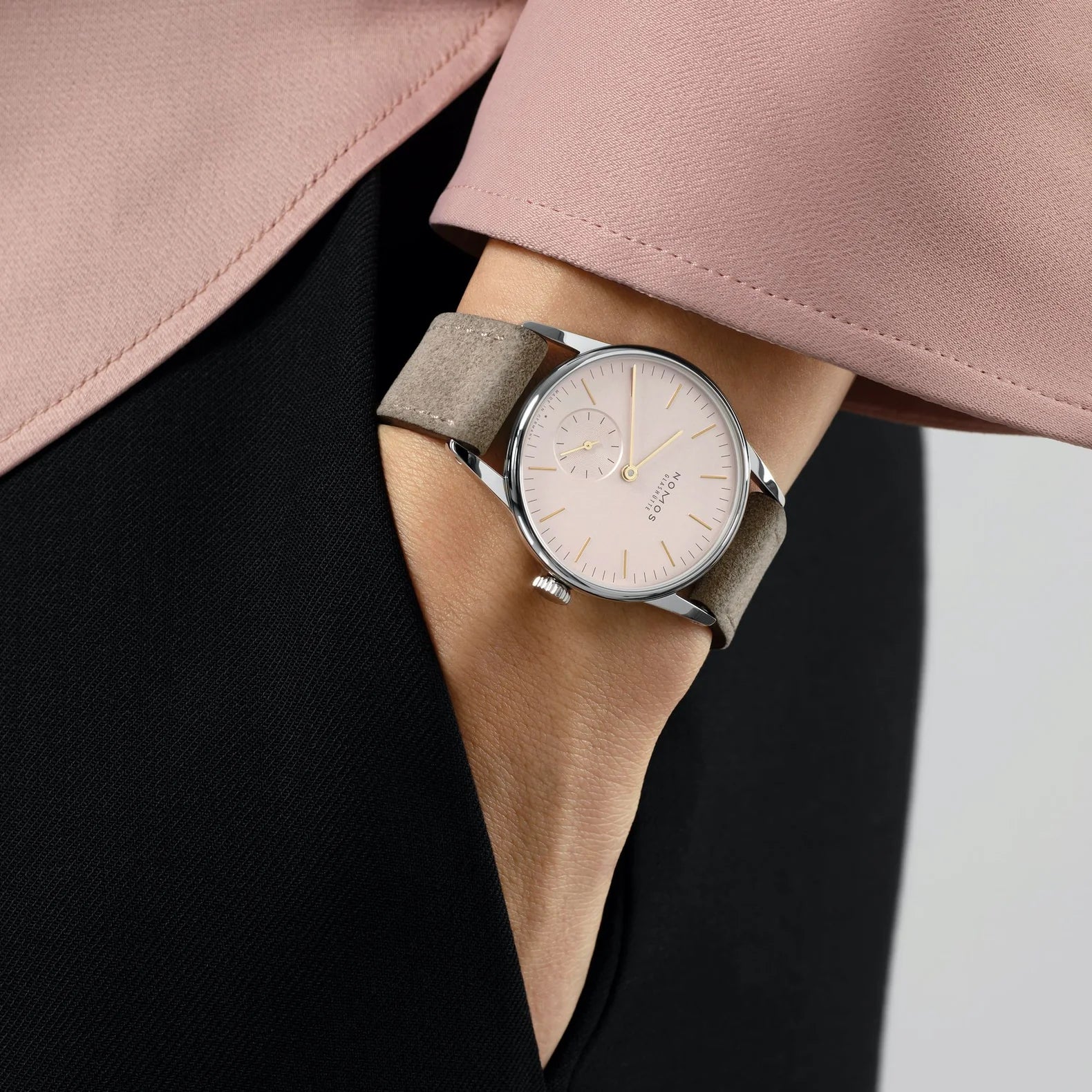 Woman wearing NOMOS Glashütte Orion 33mm watch with blush pink dial, stainless steel case, and light vegan velour strap.