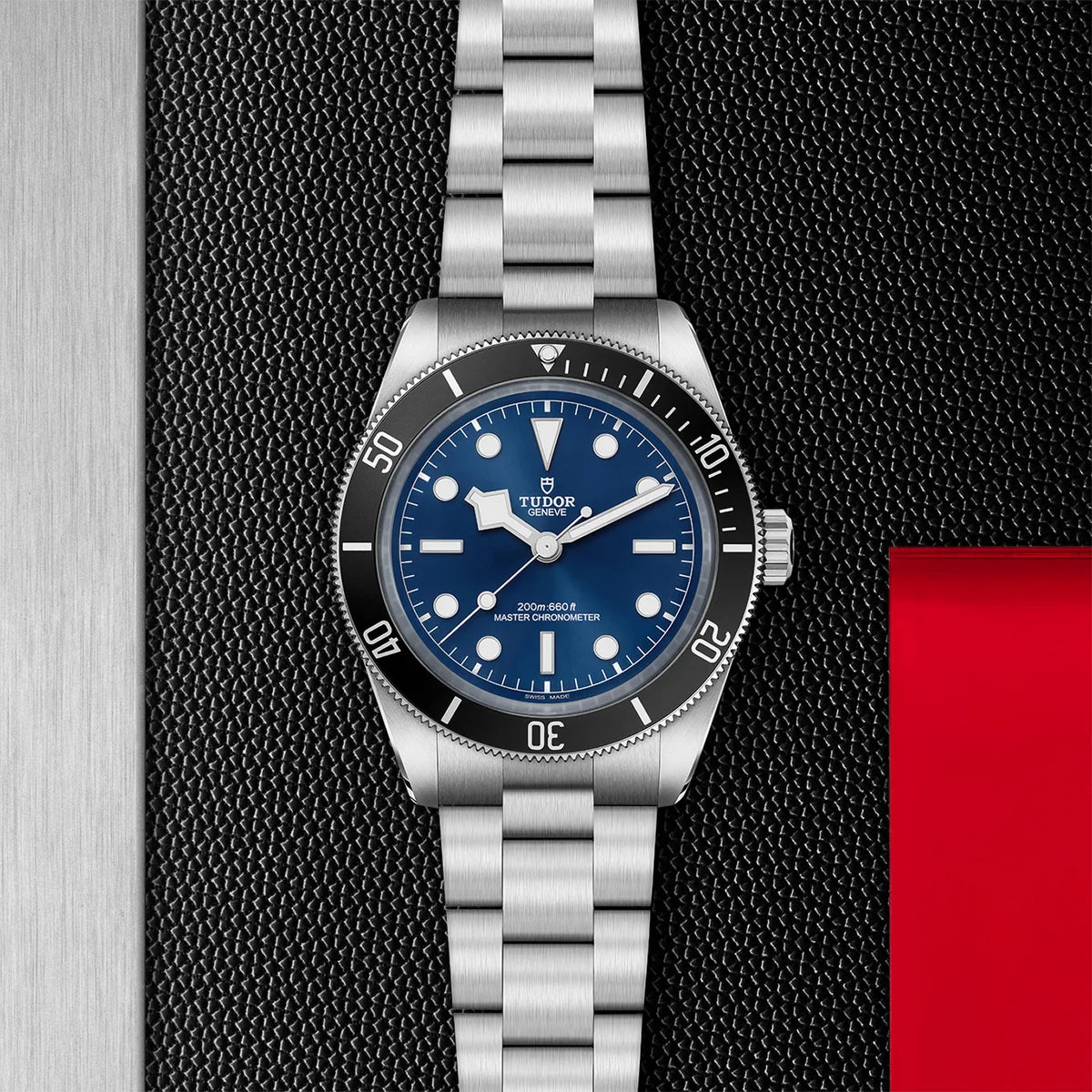 TUDOR black bay 68 43mm blue dial watch on 3-link bracelet, displayed in a top-down flat-lay composition on Tudor’s signature textured backdrop.