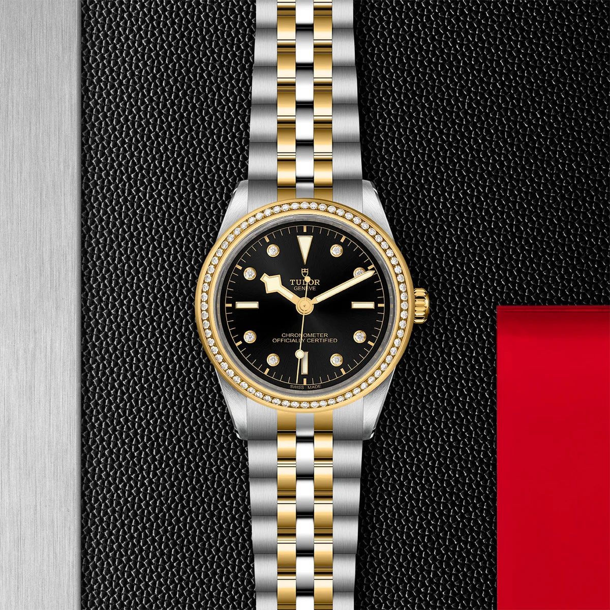 TUDOR black bay one s&g 39mm black dial watch diamond bezel on 5-link bracelet, displayed in a top-down flat-lay composition on Tudor’s signature textured backdrop.