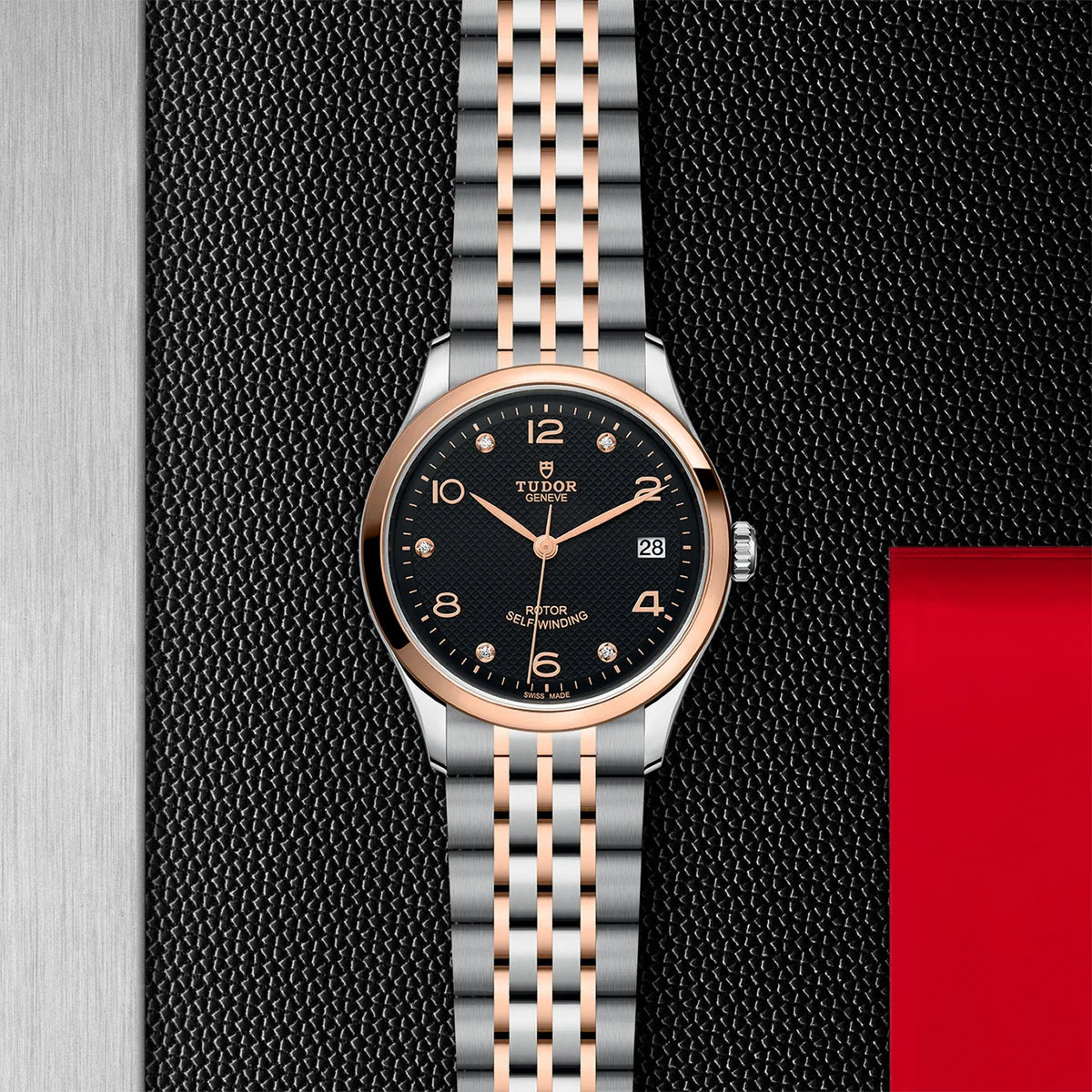 TUDOR 1926 two-tone 36mm black diamond dial watch on bracelet, displayed in a top-down flat-lay composition on Tudor’s signature textured backdrop.