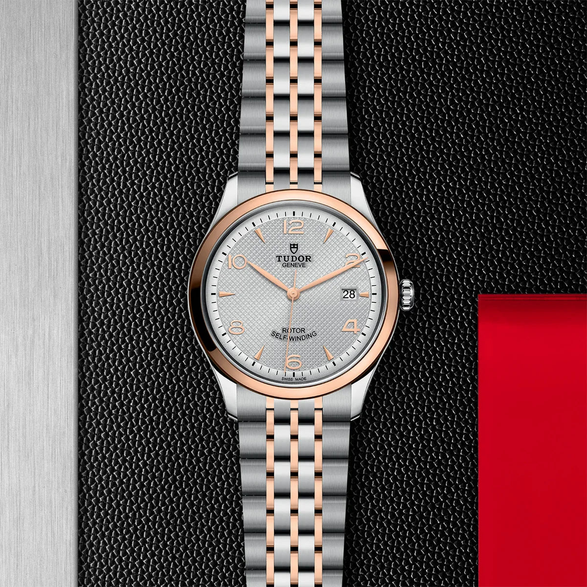 TUDOR 1926 two-tone 39mm silver dial watch on bracelet, displayed in a top-down flat-lay composition on Tudor’s signature textured backdrop.