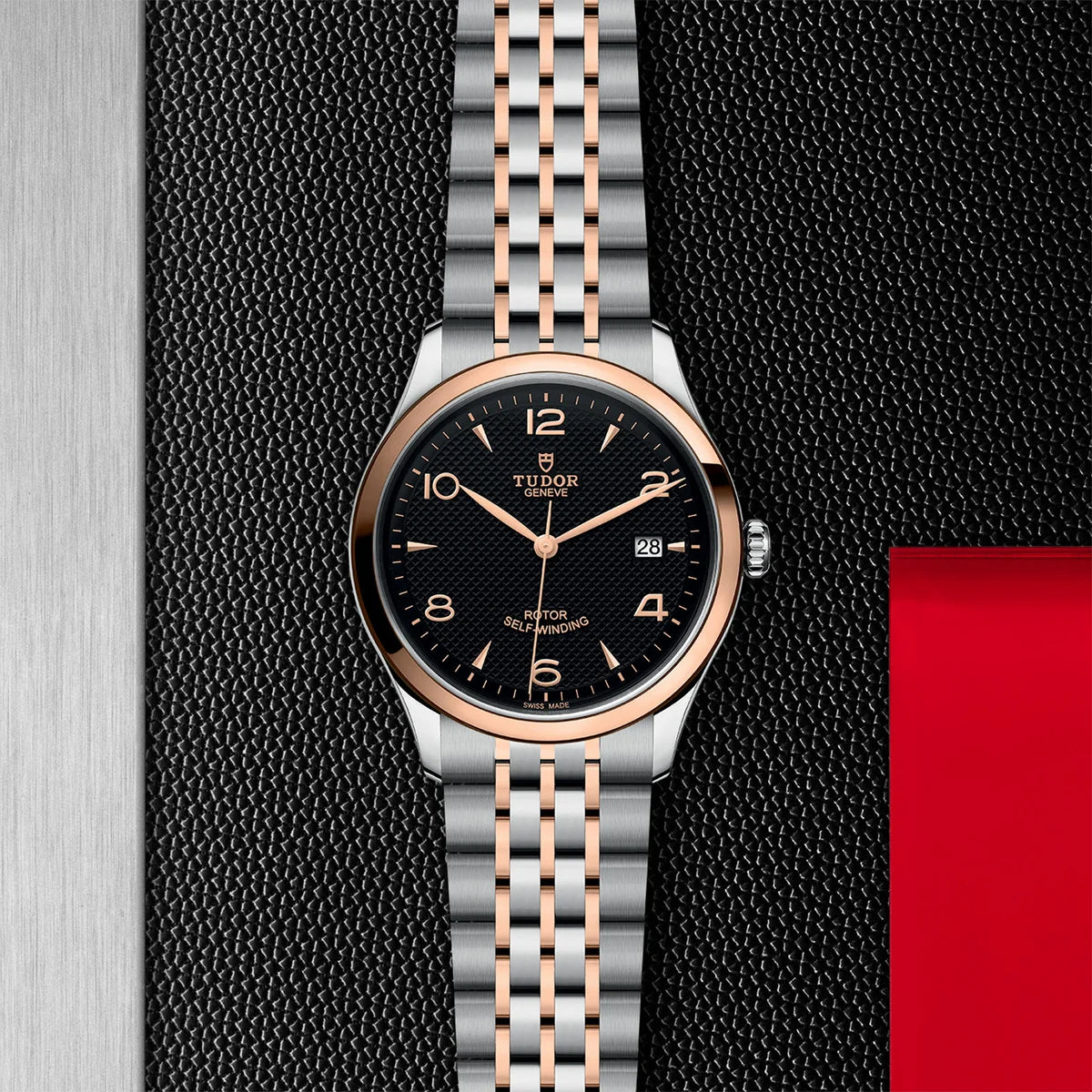 TUDOR 1926 two-tone 39mm black dial watch on bracelet, displayed in a top-down flat-lay composition on Tudor’s signature textured backdrop.