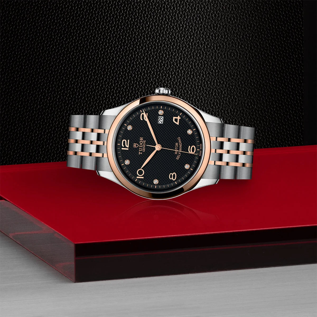 TUDOR 1926 two-tone 39mm black diamond dial watch on bracelet, shown laying on its side on Tudor’s signature red platform.
