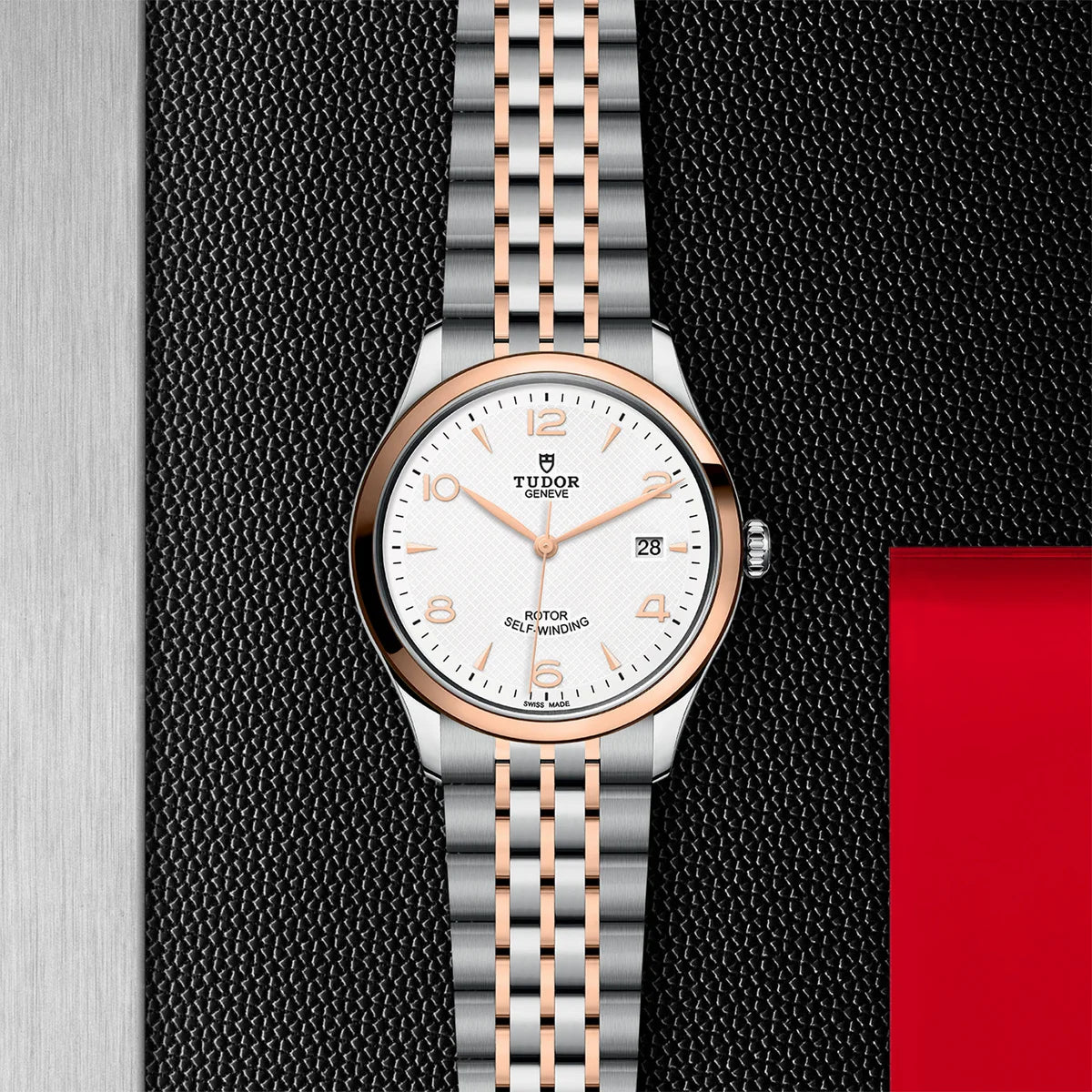 TUDOR 1926 two-tone 39mm white dial watch on bracelet, displayed in a top-down flat-lay composition on Tudor’s signature textured backdrop.