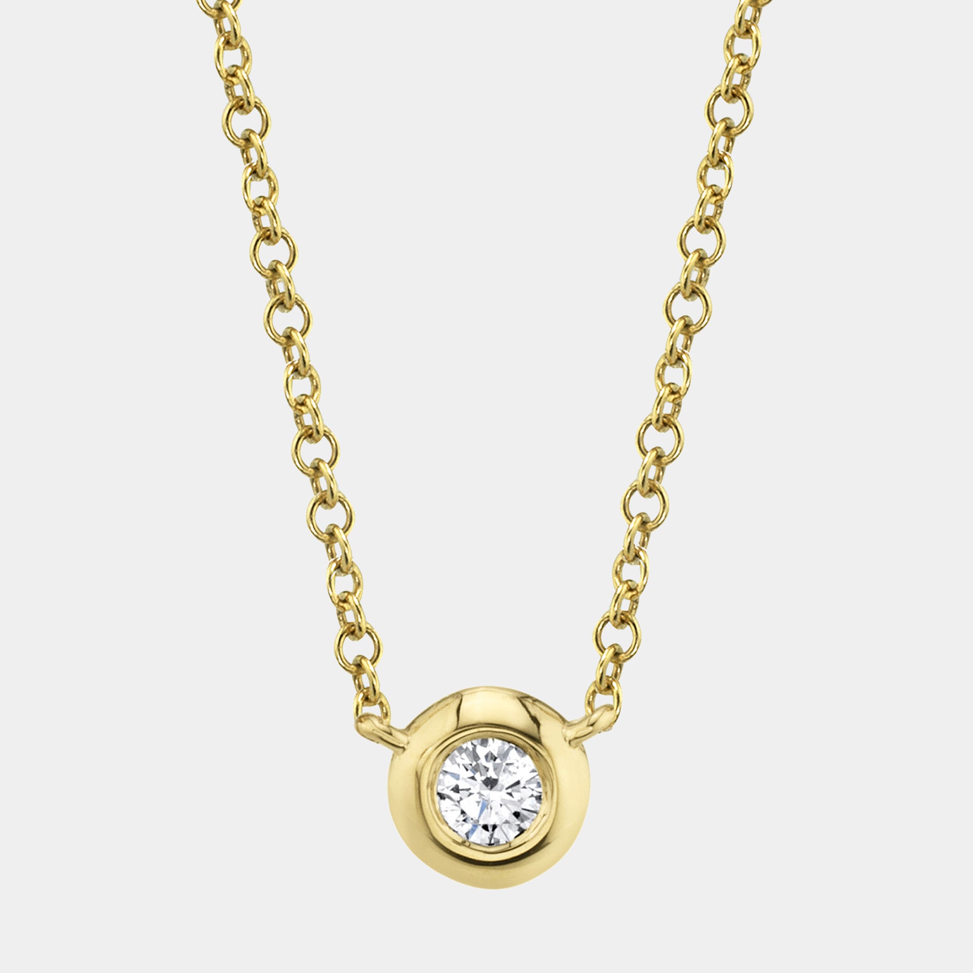 Gold necklace with a diamond bezel pendant on a light gray background