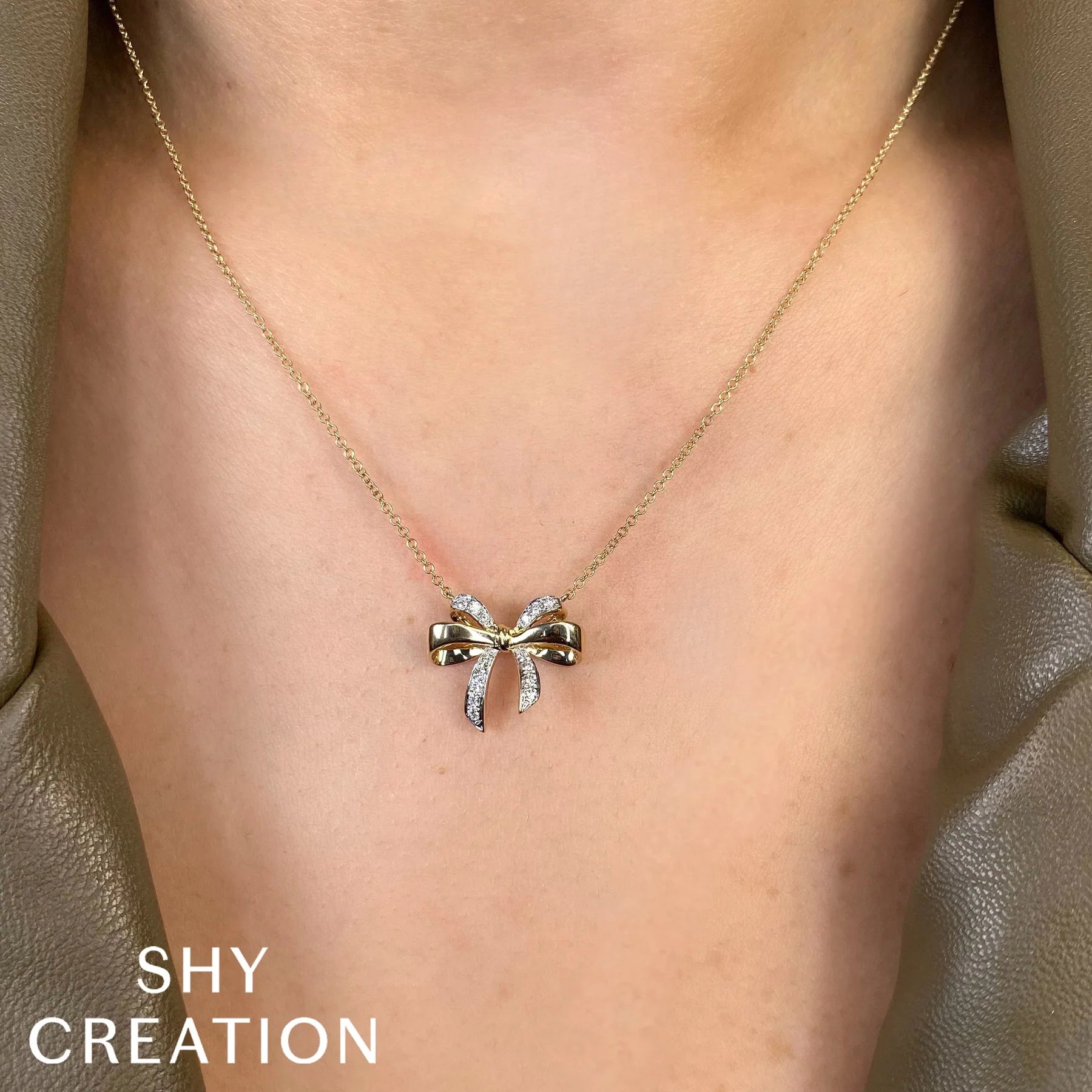 Gold bow-shaped necklace on a person's neck with 'SHY CREATION' branding.