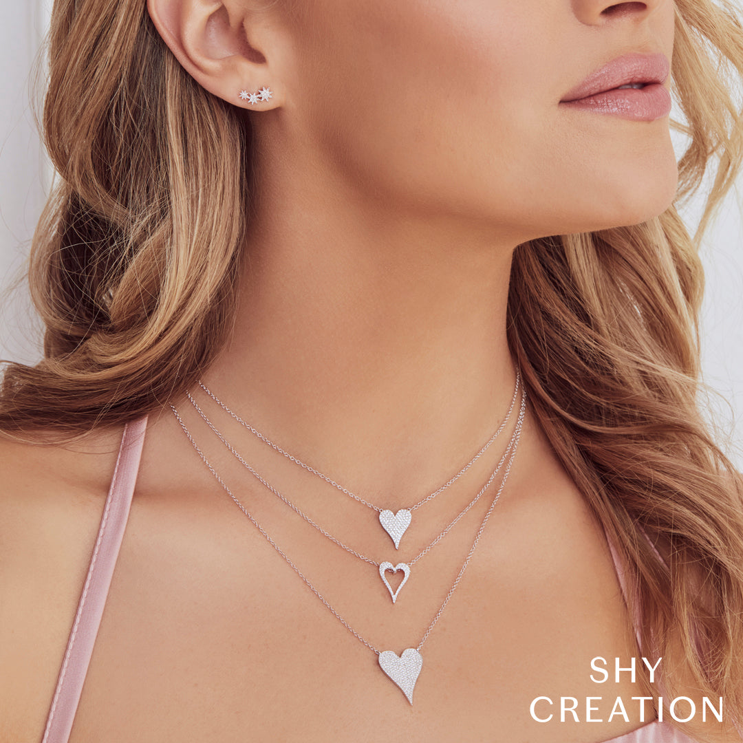 Woman wearing heart-shaped diamond necklaces and earrings with 'SHY CREATION' branding.
