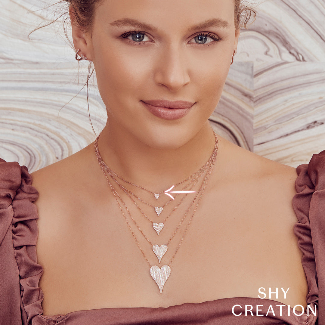 Woman wearing a necklace with heart pendants against a neutral background, branded 'SHY CREATION'.