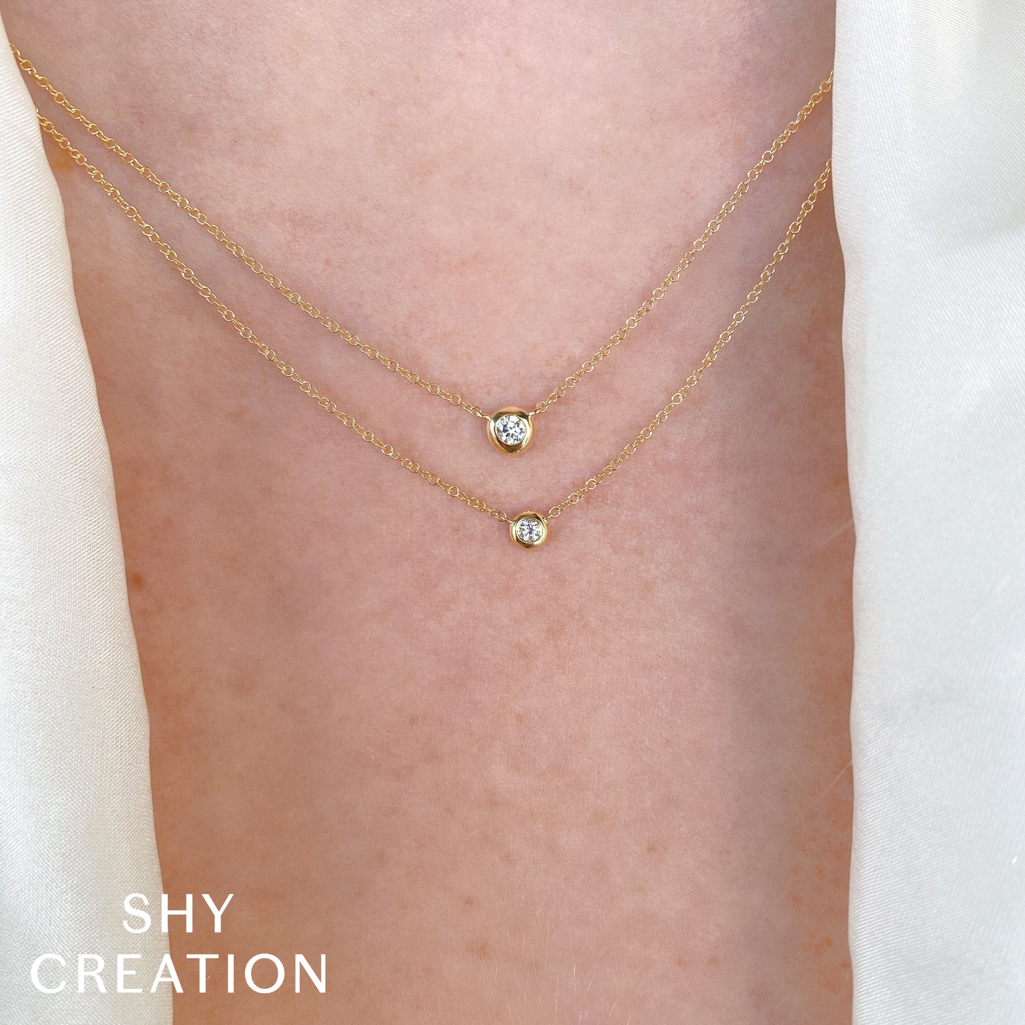 Gold necklace with small diamonds on a person's neck, branded 'SHY CREATION'.