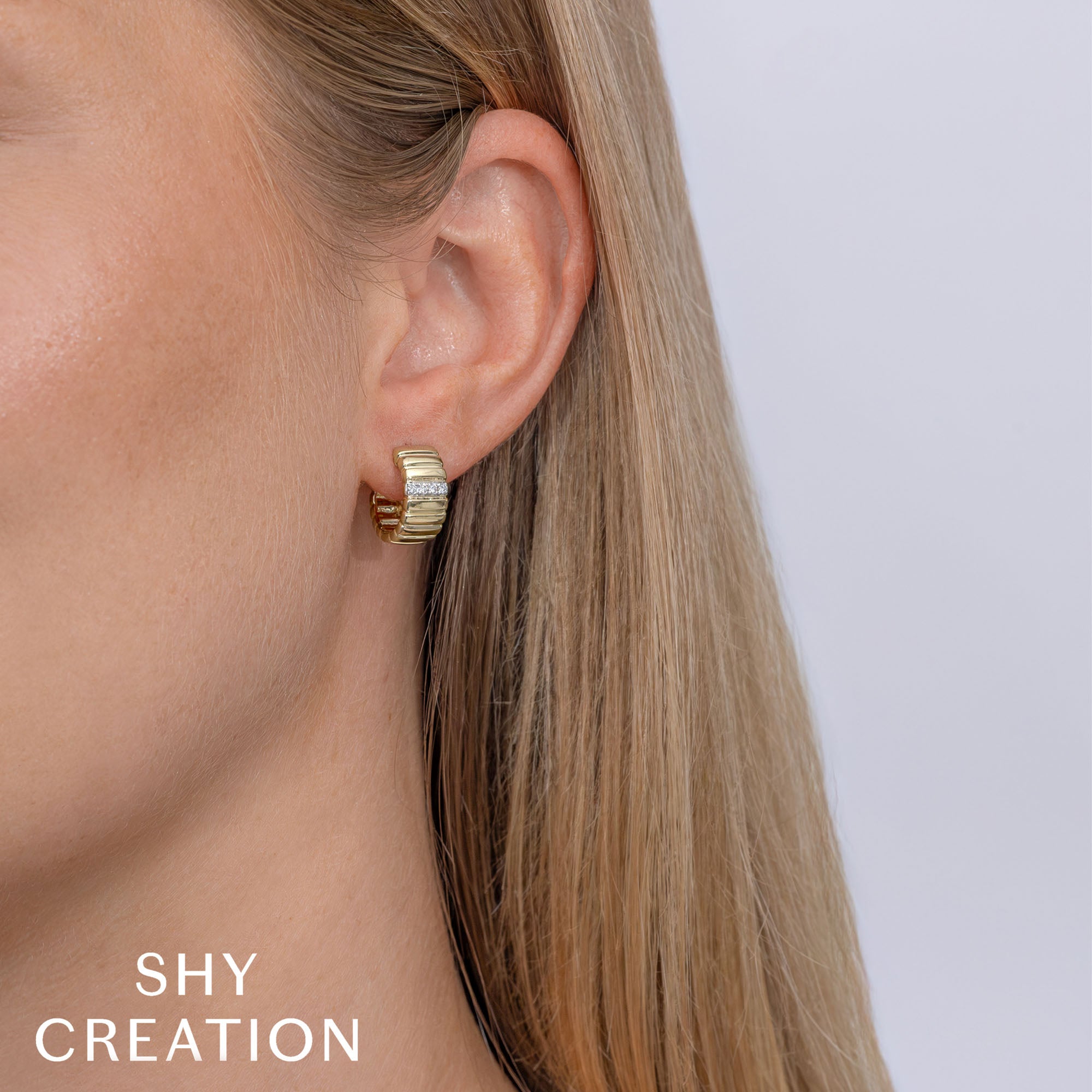 Woman wearing yellow gold diamond ribbed huggie earrings