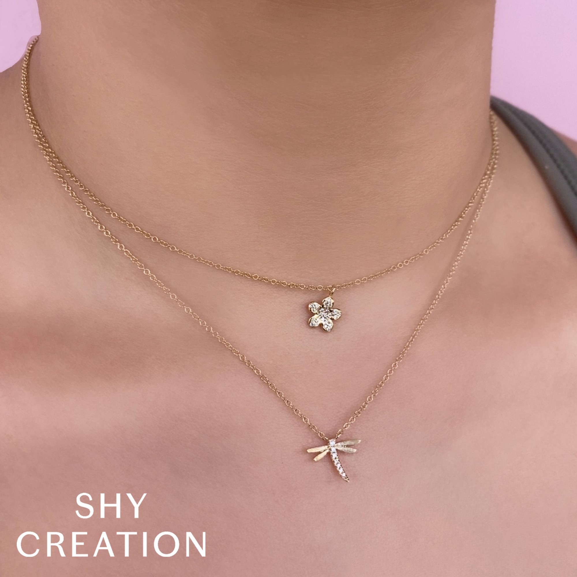 Two delicate necklaces with floral and dragonfly pendants on a person's neck, branded 'SHY CREATION'.