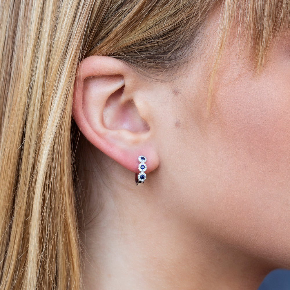 Woman wearing white gold sapphire and diamond huggie earrings