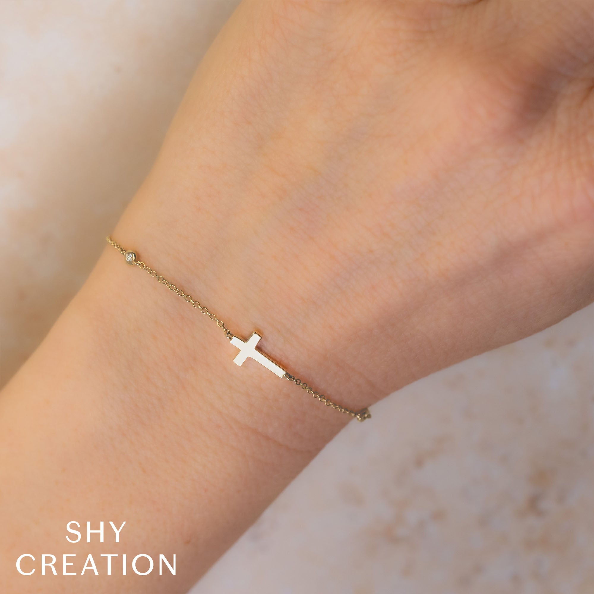 Woman wearing yellow gold diamond cross charm bracelet, wrist closeup