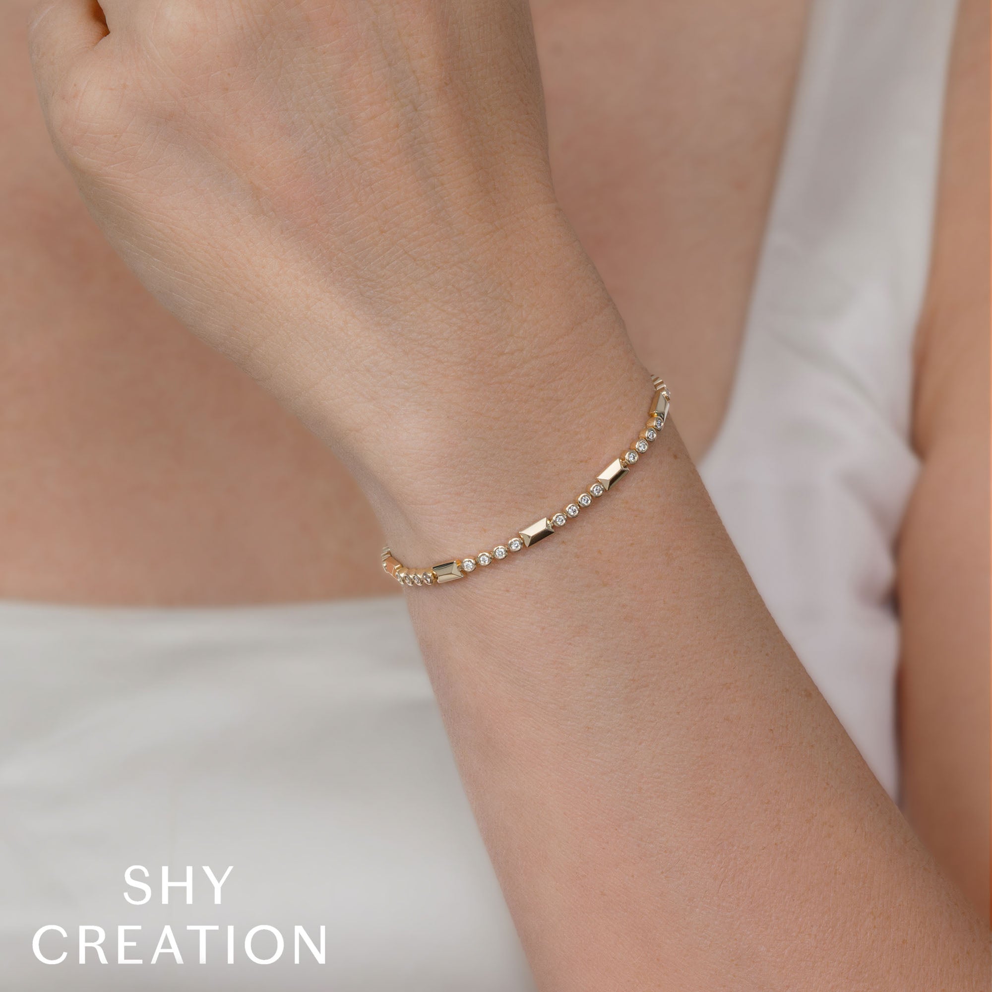 Woman wearing yellow gold geo cut diamond tennis bracelet, wrist closeup