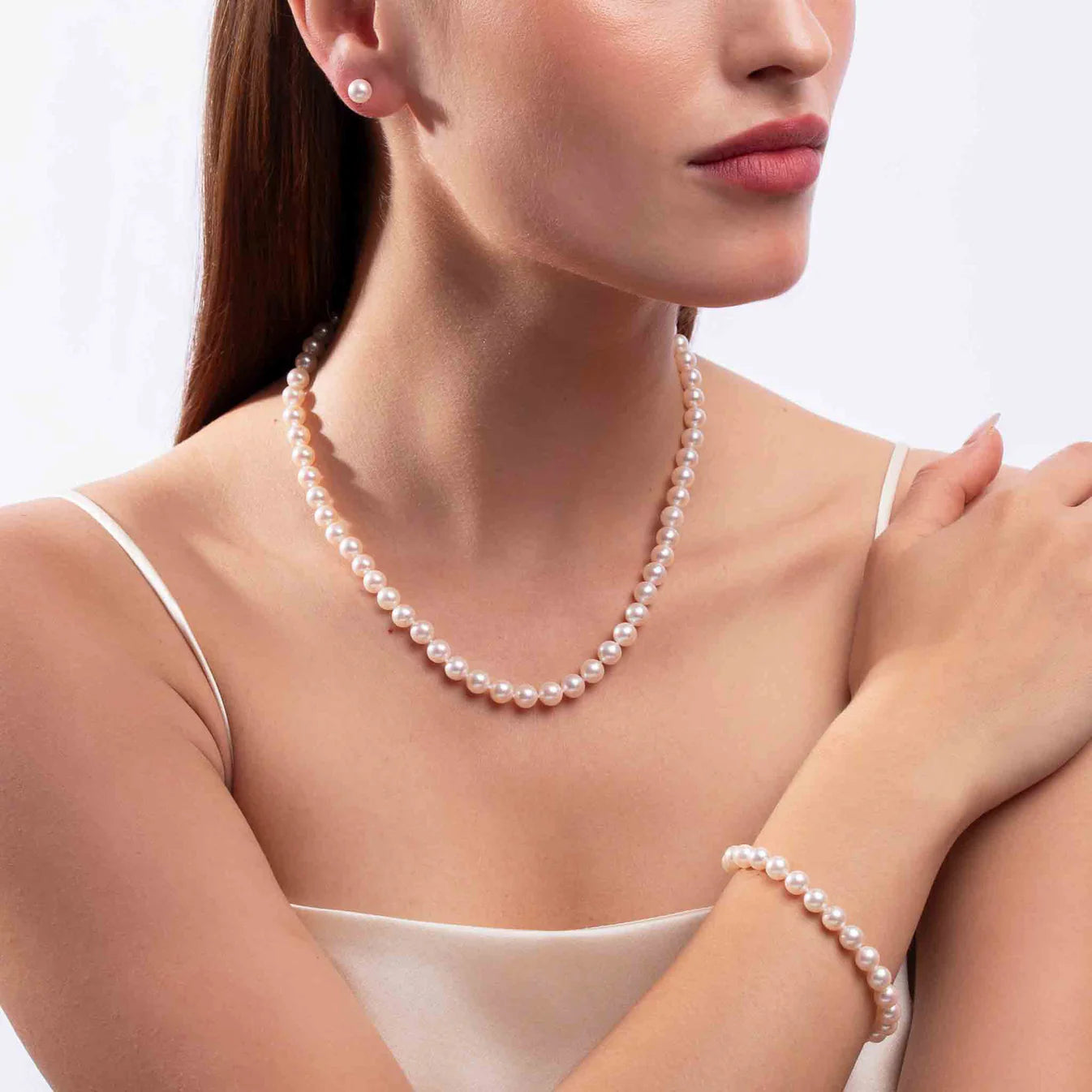 Woman wearing pearl necklace, bracelet, and earrings set on a light gray background
