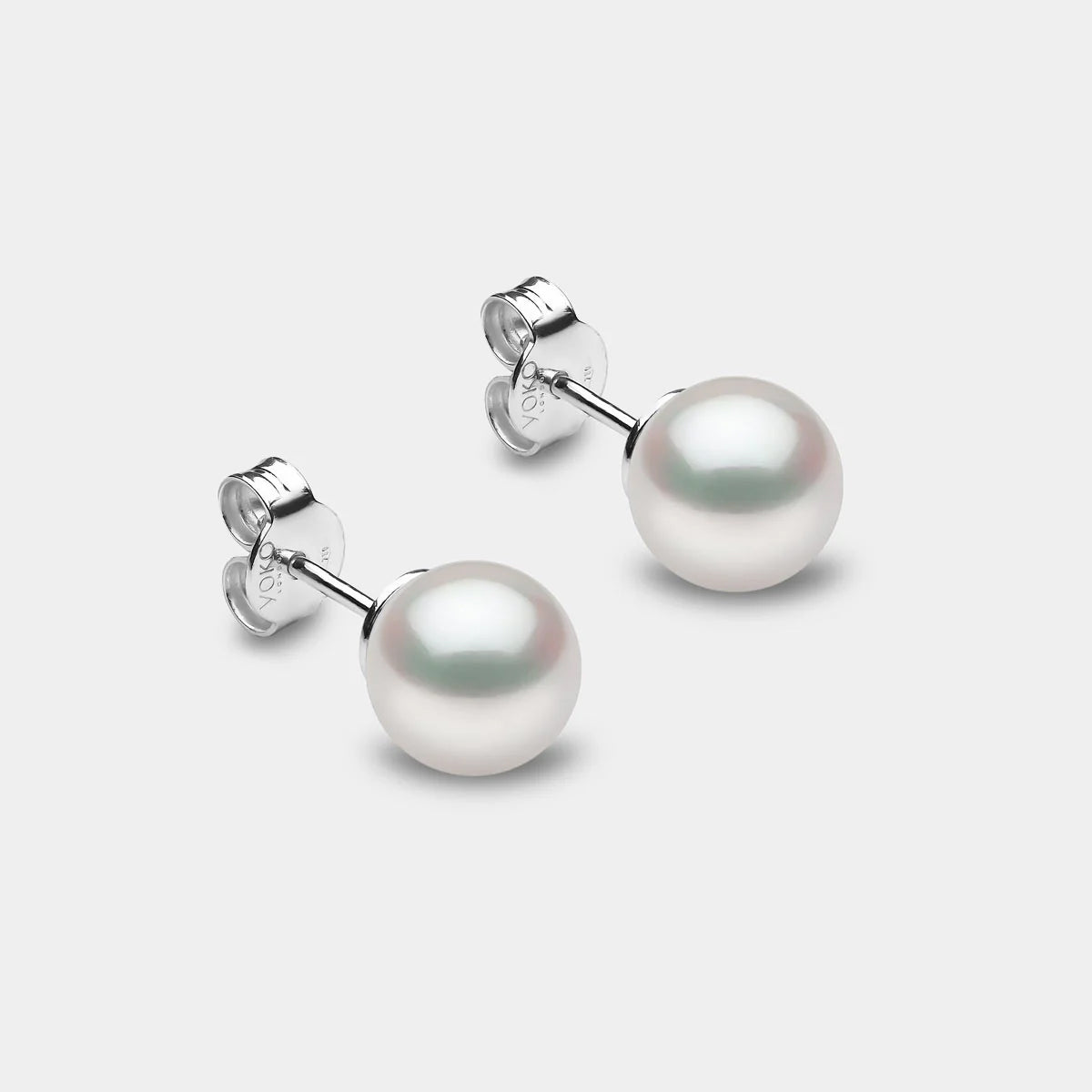 Pair of pearl earrings on a light gray background, side angle view