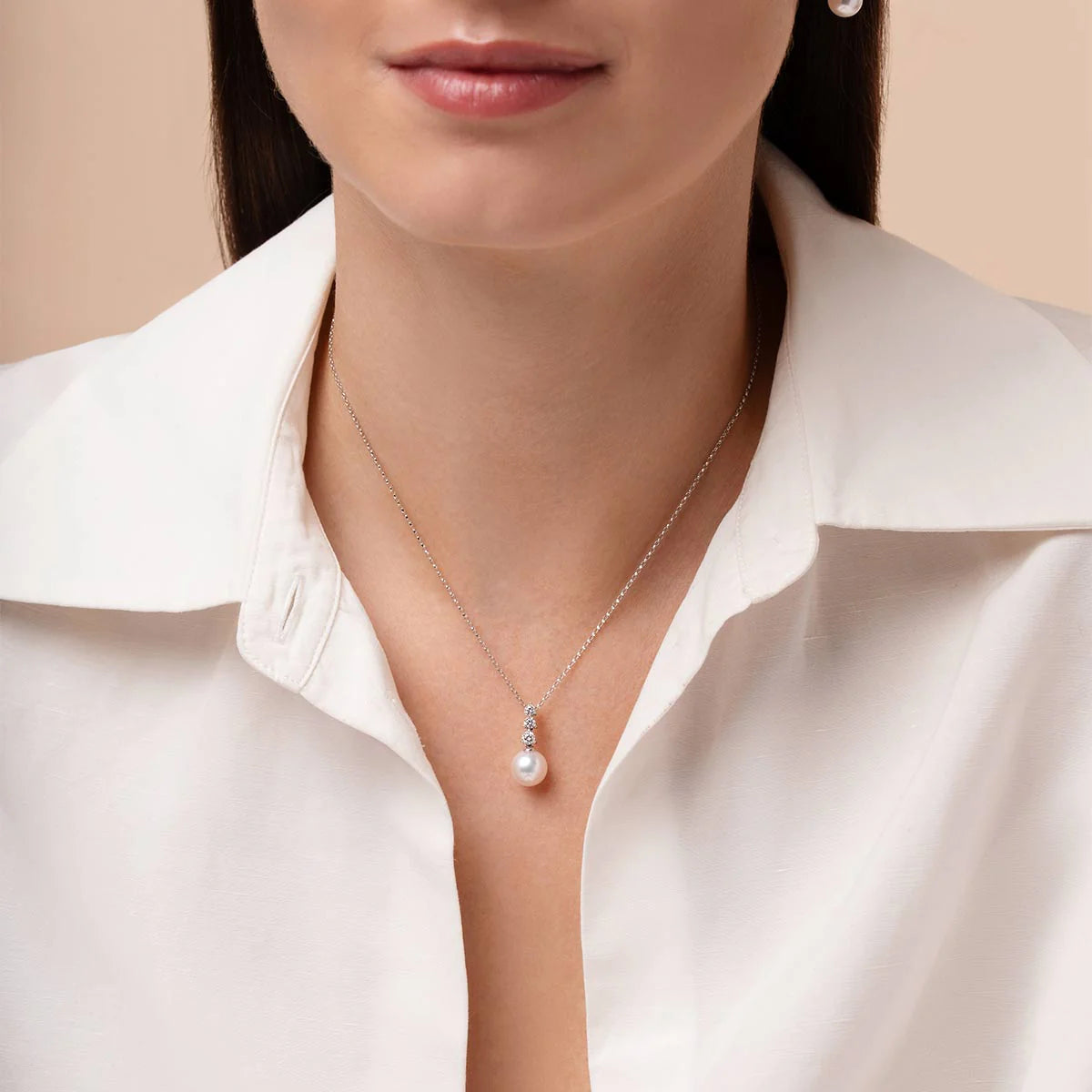Woman wearing white gold pearl pendant necklace with three diamond accents