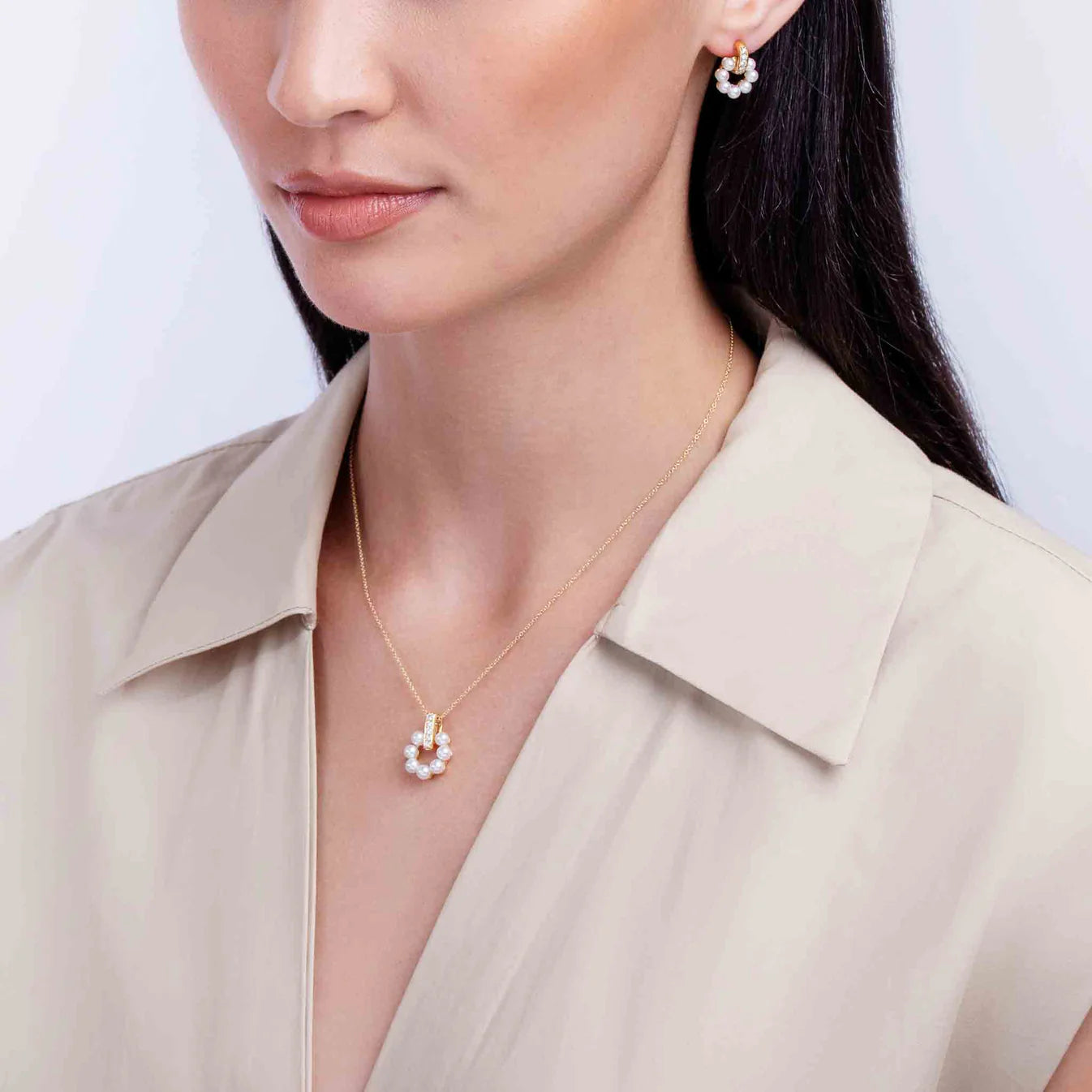 Woman wearing a gold necklace with a pearl and diamond pendant against a plain background