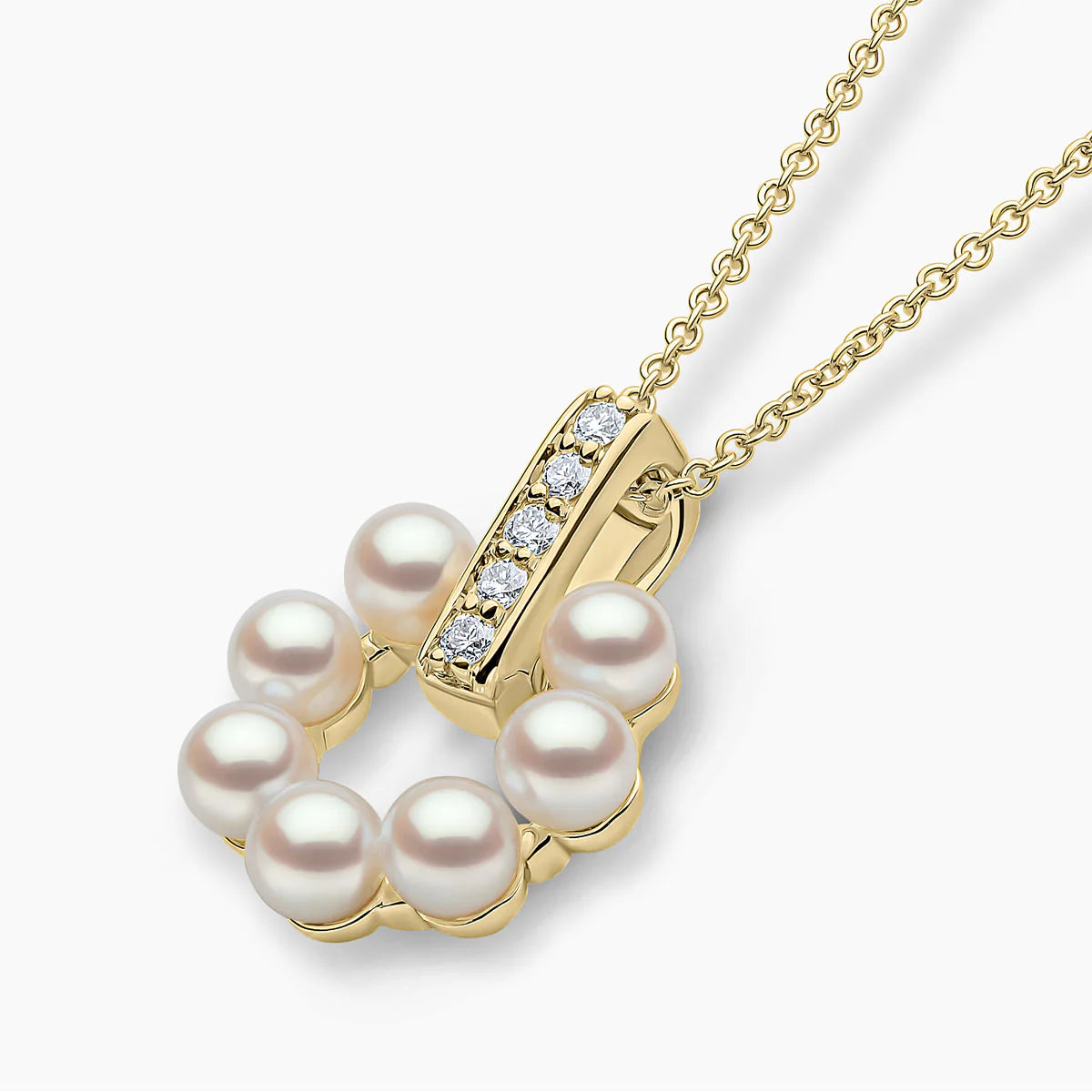 Yellow gold pearl pendant with diamond accents on grey background, side angle view