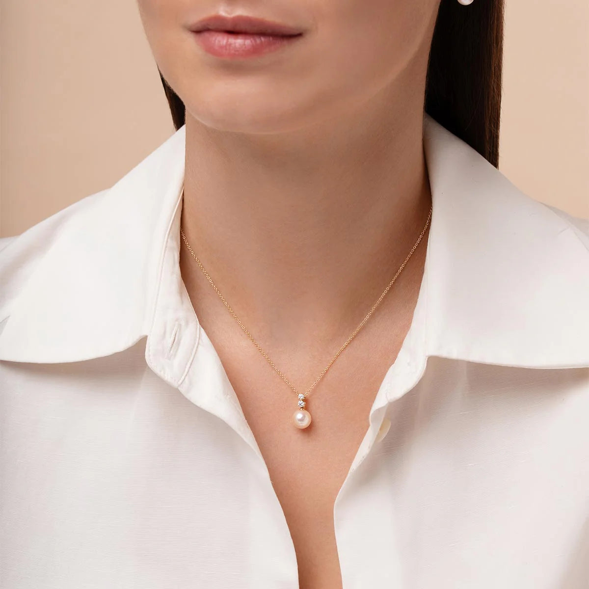 Pearl necklace worn by a woman in a white shirt against a beige background