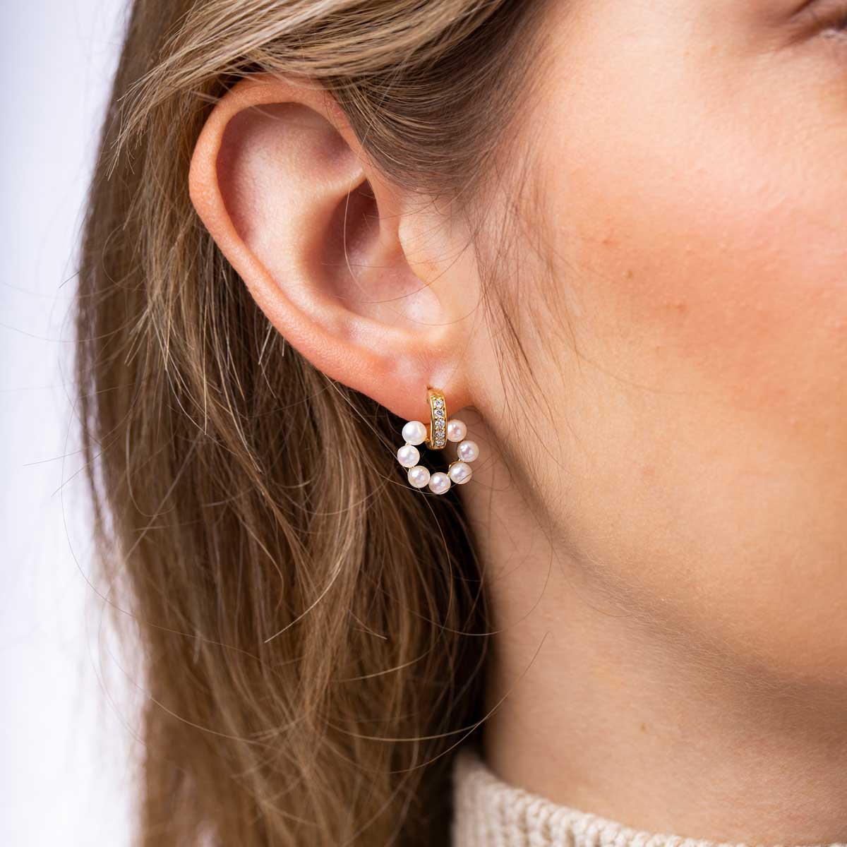 Close-up of an ear wearing a pearl earring with a white background