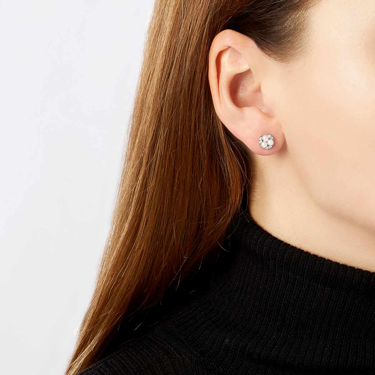 Woman wearing white gold pearl and diamond stud earrings in black turtleneck sweater