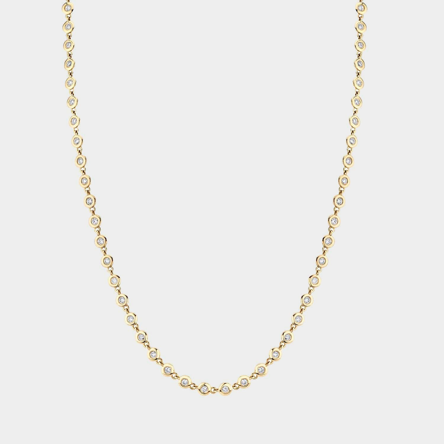 Yellow gold bezel set diamond tennis necklace on grey background