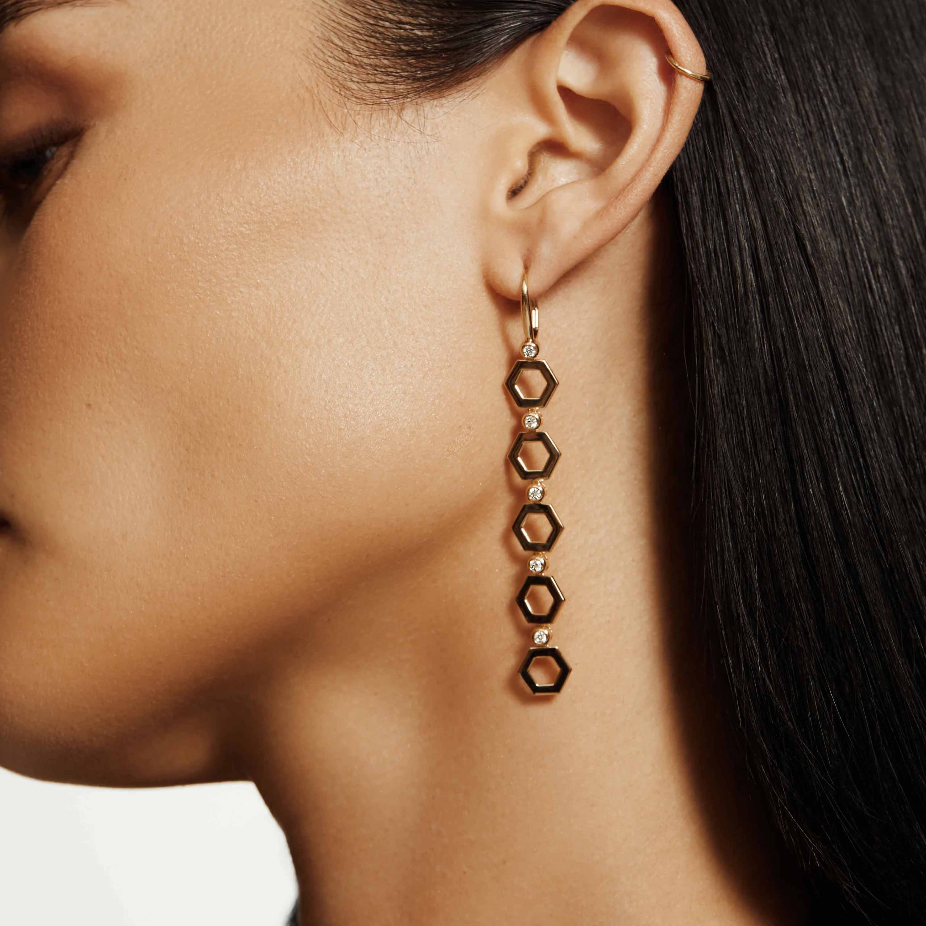 Woman wearing yellow gold hex infinity drop earrings on grey background