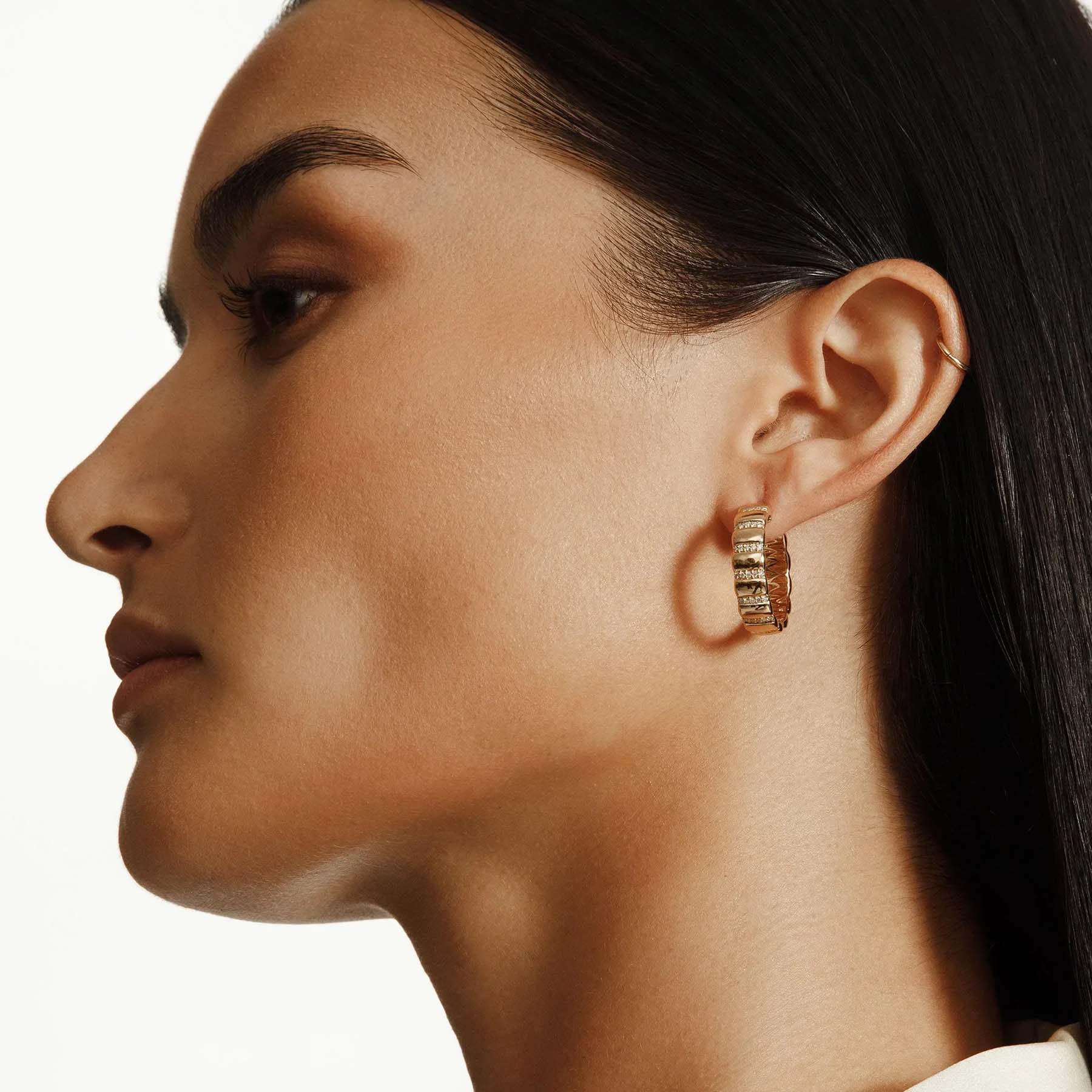 Woman wearing yellow gold and diamond ribbed huggie earrings