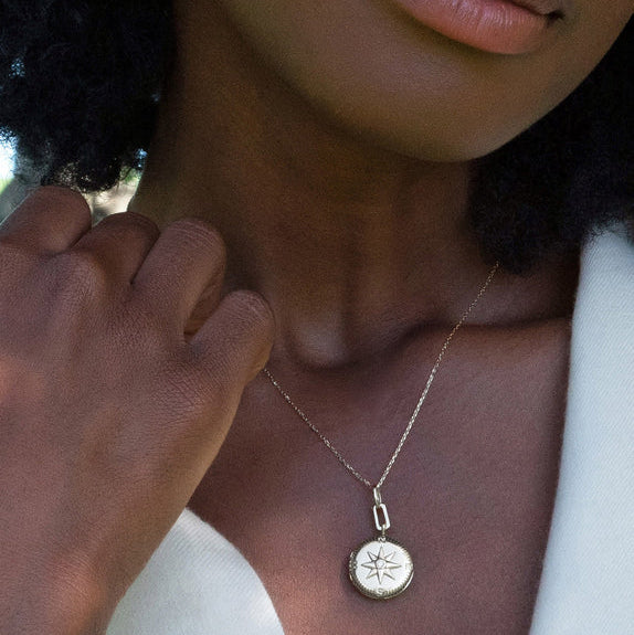 Woman wears silver pendant necklace with compass and two photos