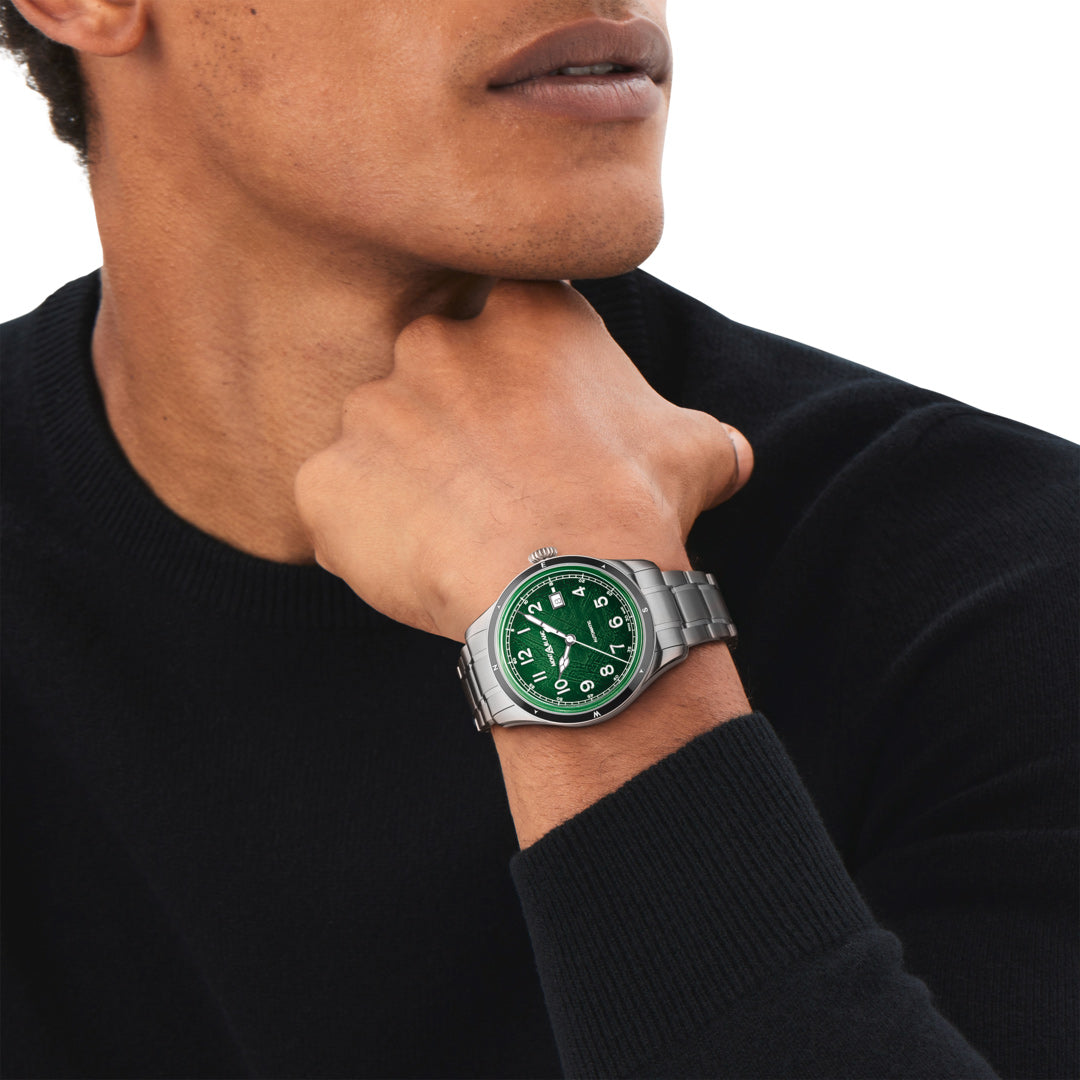 Person wearing a watch with a green face and silver case, against a neutral background