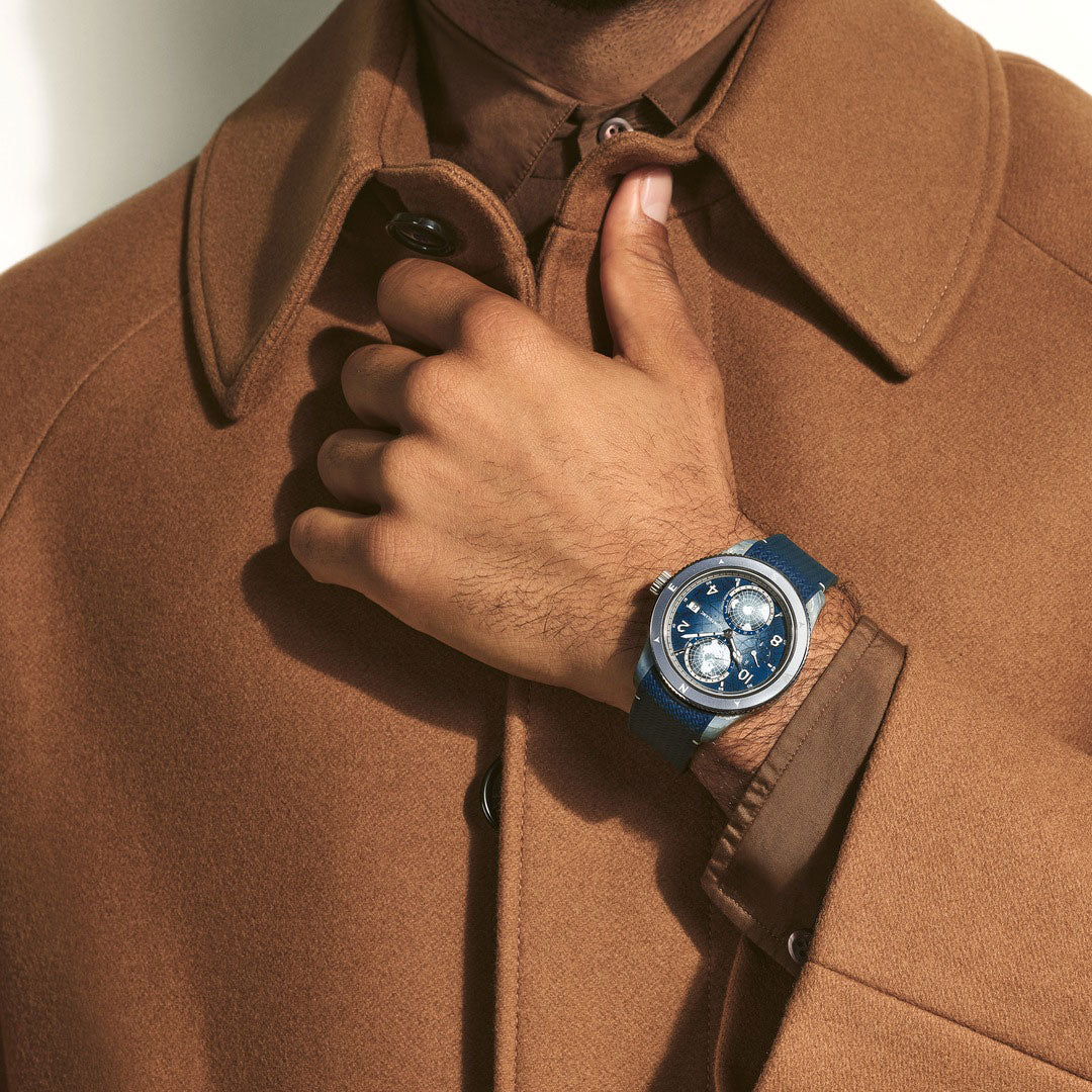 Person wearing a brown coat with a hand adjusting the collar, wearing a blue watch.