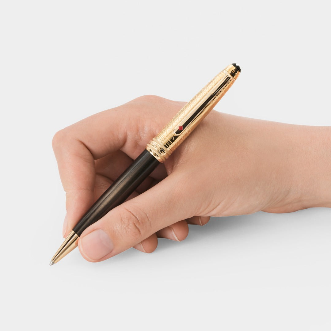 Hand holding a pen with a gold and black design on a light background